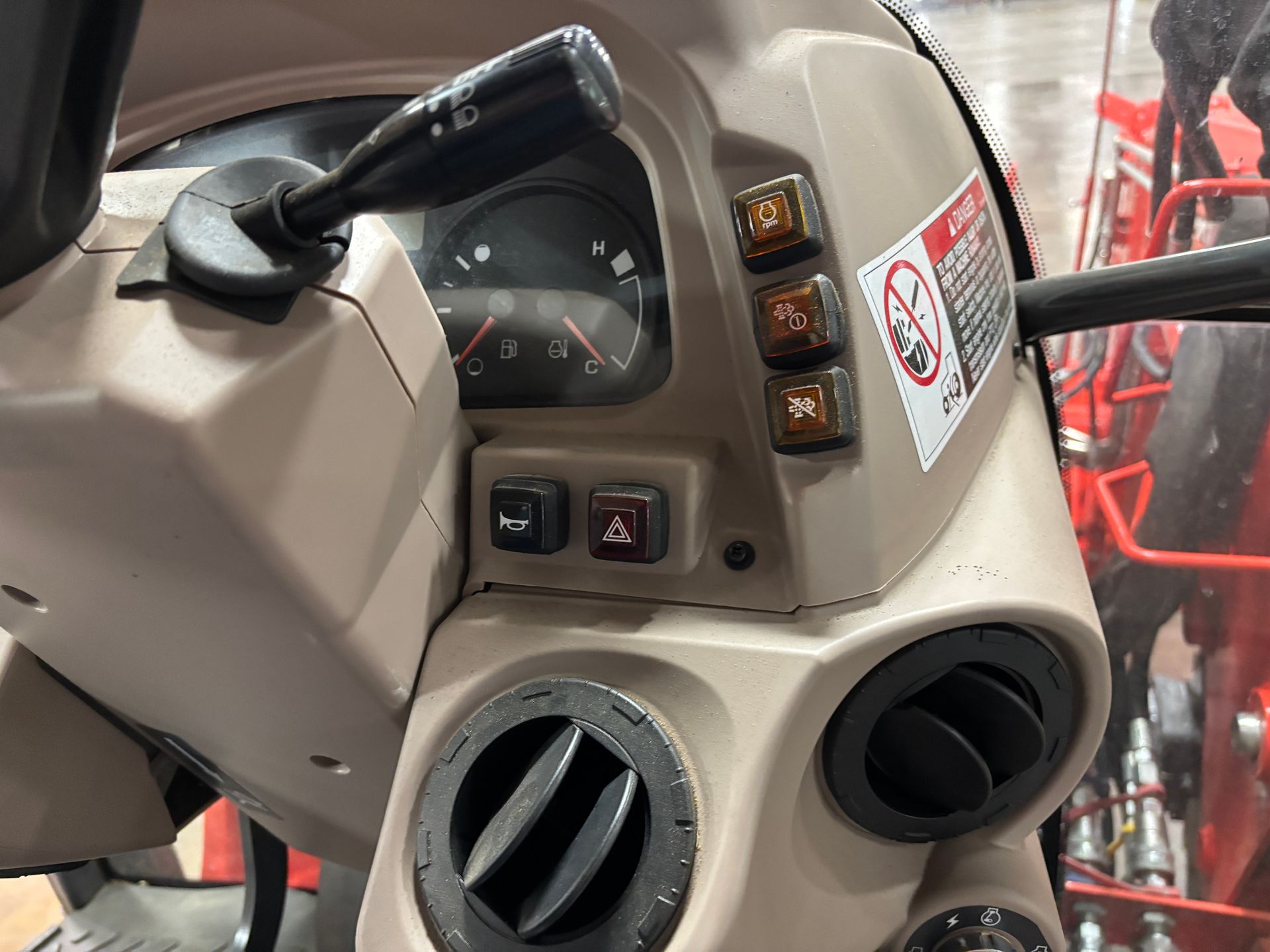 Dashboard of a tractor, showing gauges, lights, and air vents. Beige plastic. Black controls. Warning sticker.