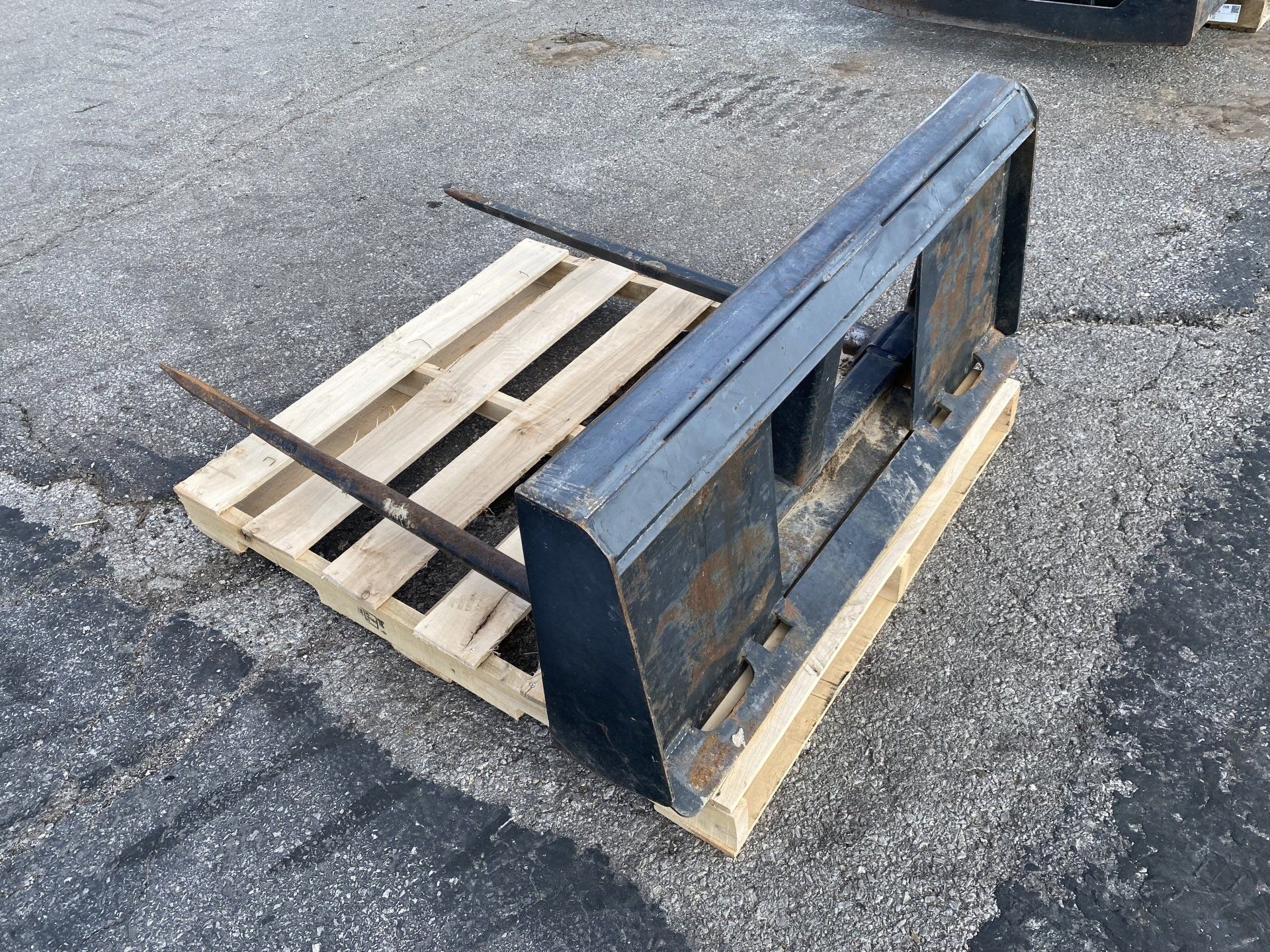 Forklift forks resting on top of a wooden pallet, on a concrete surface.