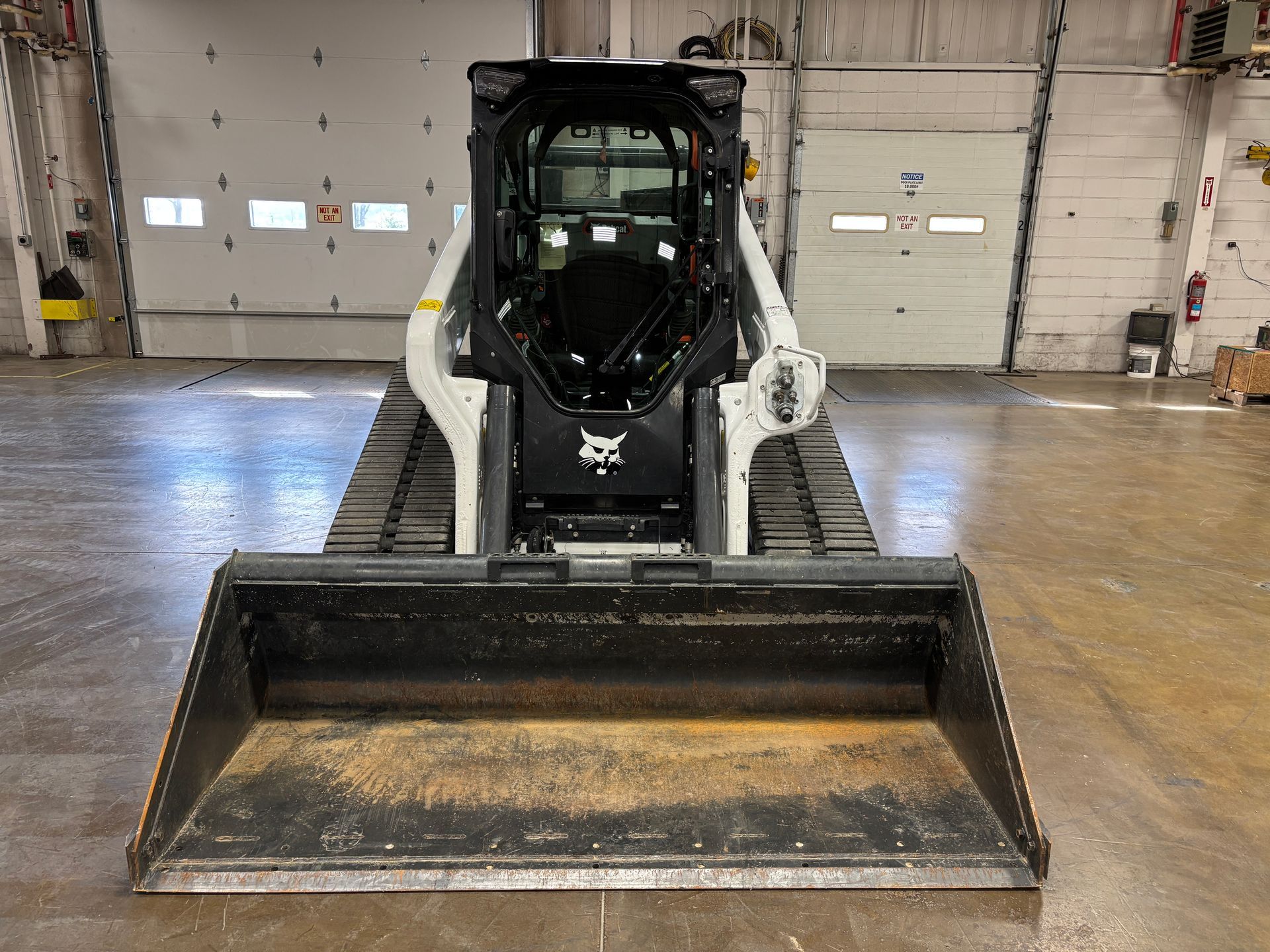 Bobcat compact track loader with a large bucket, black and white, indoors.