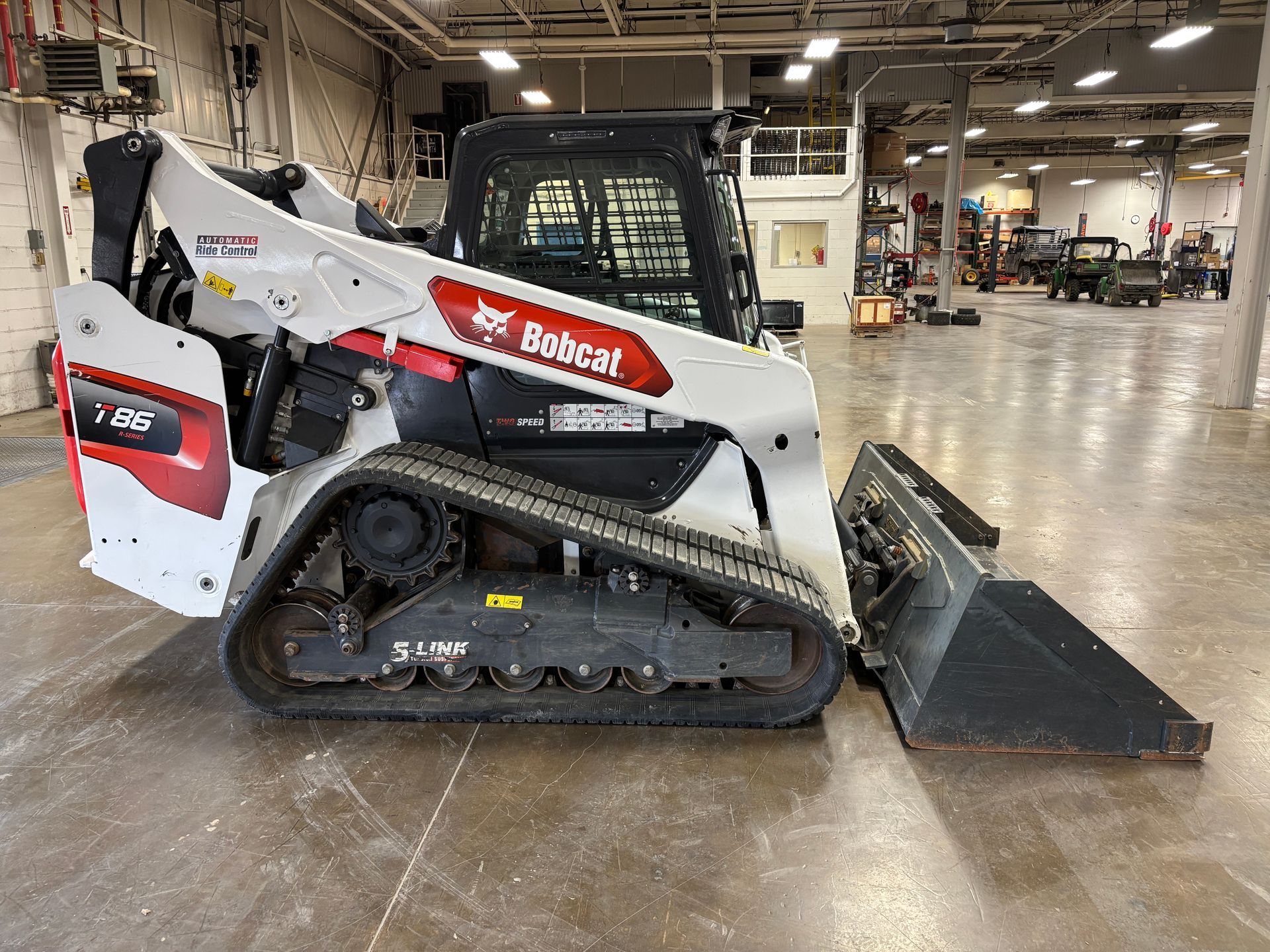 White Bobcat compact track loader with bucket in a warehouse, side view shot.
