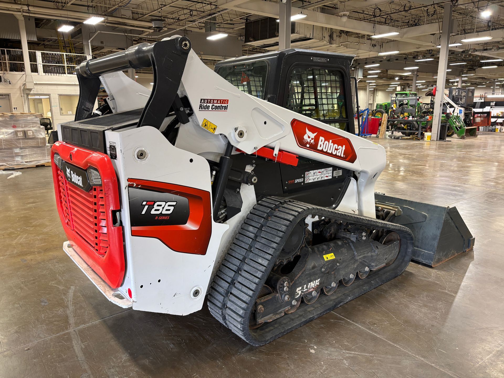 White Bobcat compact track loader with bucket in a warehouse, back angled shot.