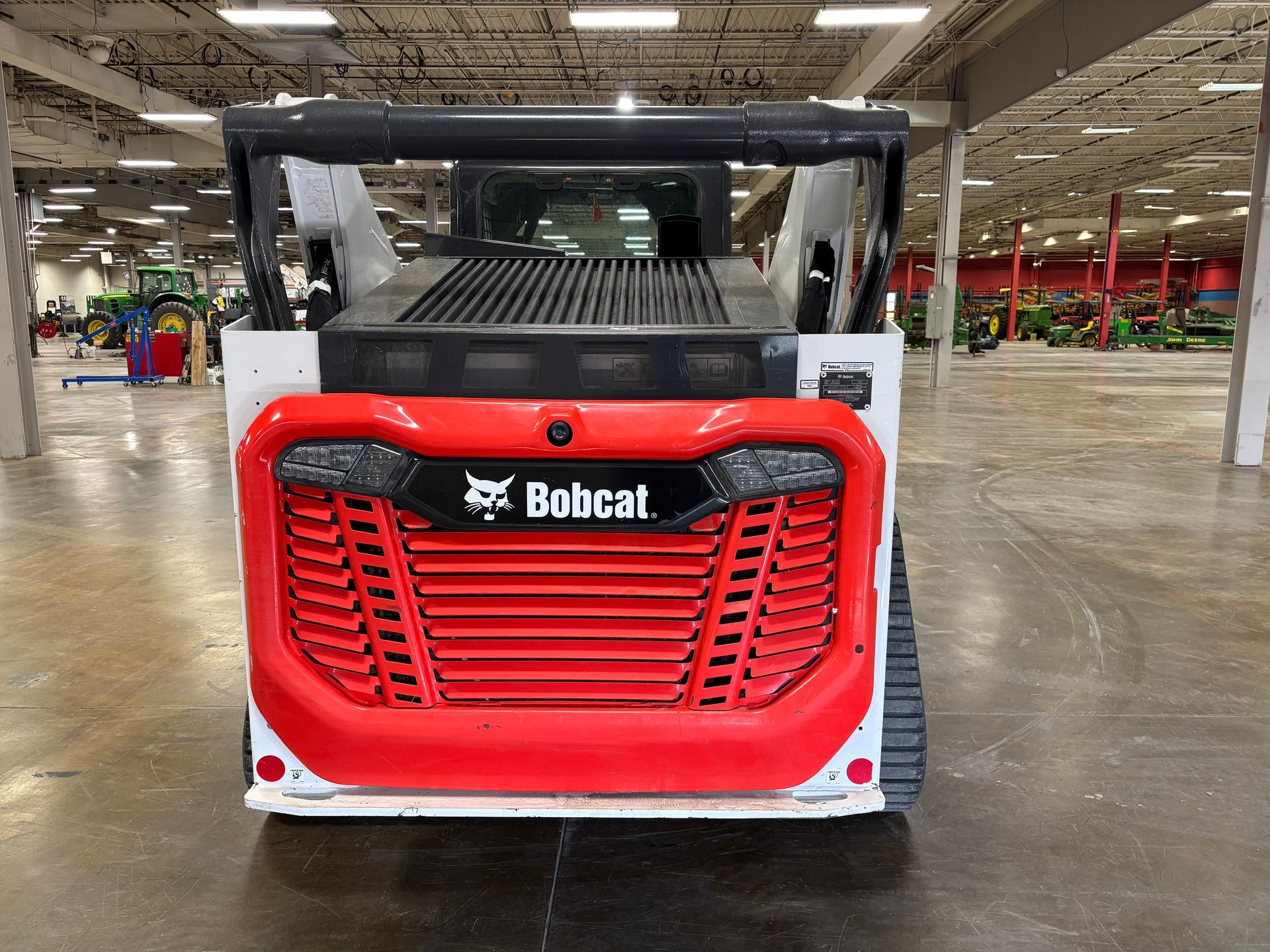 White Bobcat compact track loader with bucket in a warehouse, back shot.