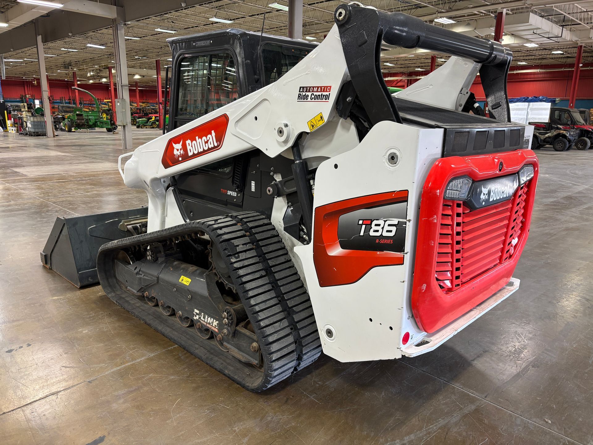 White Bobcat compact track loader with bucket in a warehouse, back angled shot.