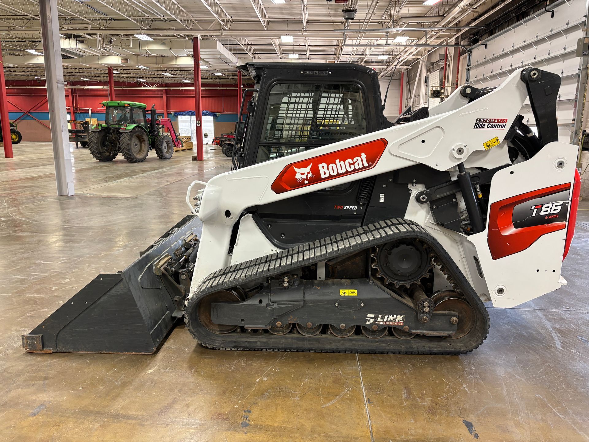 White Bobcat compact track loader with bucket in a warehouse, side view shot.