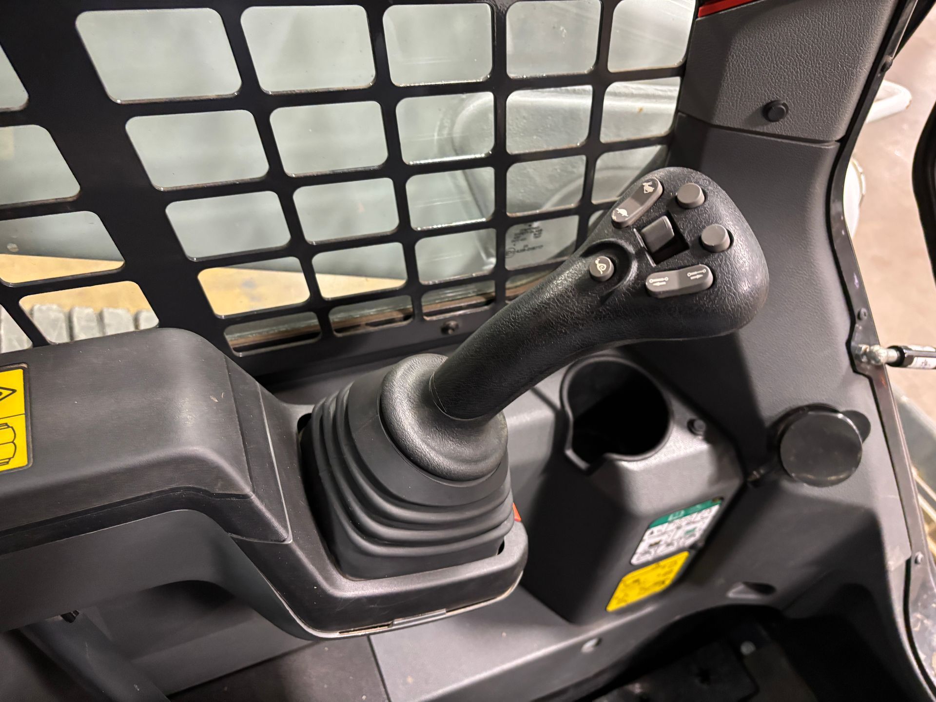Black joystick control inside a compact track loader cab, with buttons and cup holder.