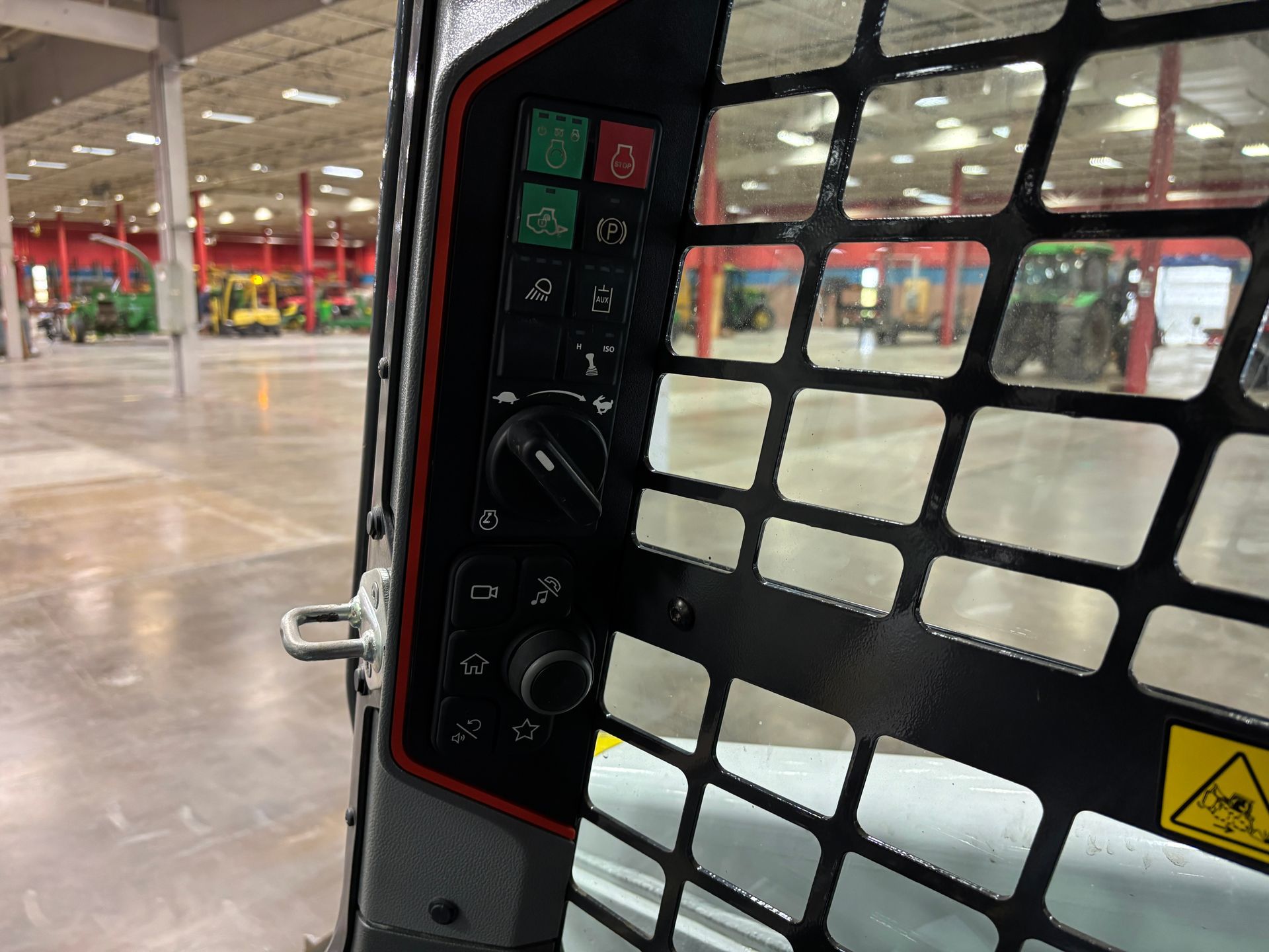 Control panel inside a compact track loader cab, with buttons, dials, and a safety cage.