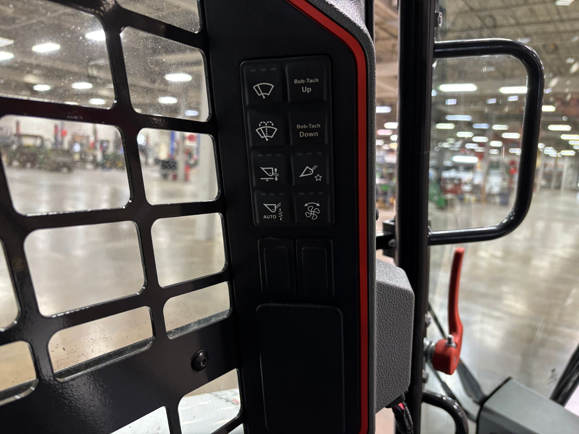 Black control panel with six buttons on a compact track loader, next to a safety screen.