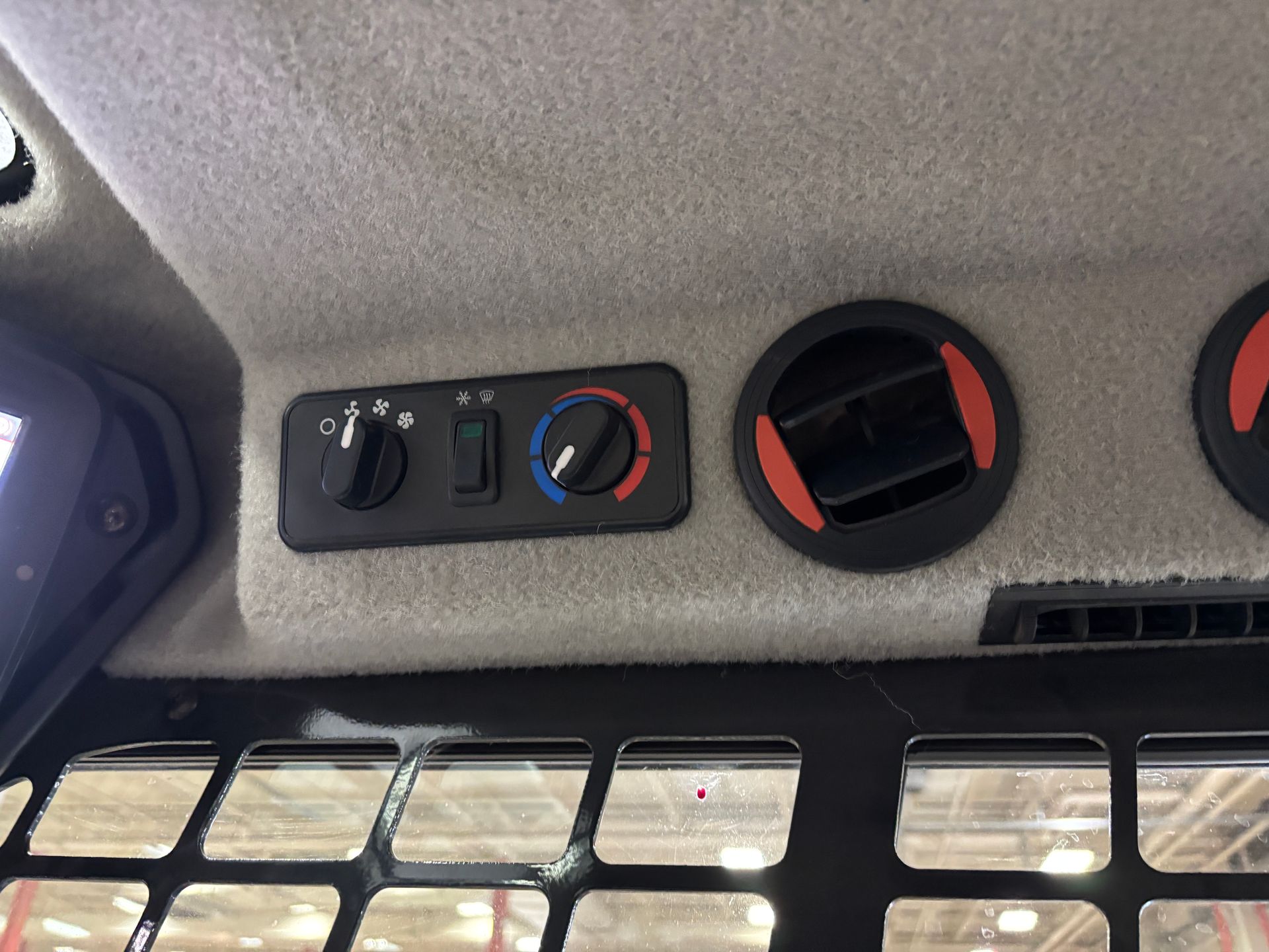 Controls for a compact track loader climate, with black dials and a rectangular panel, mounted on a light gray interior.