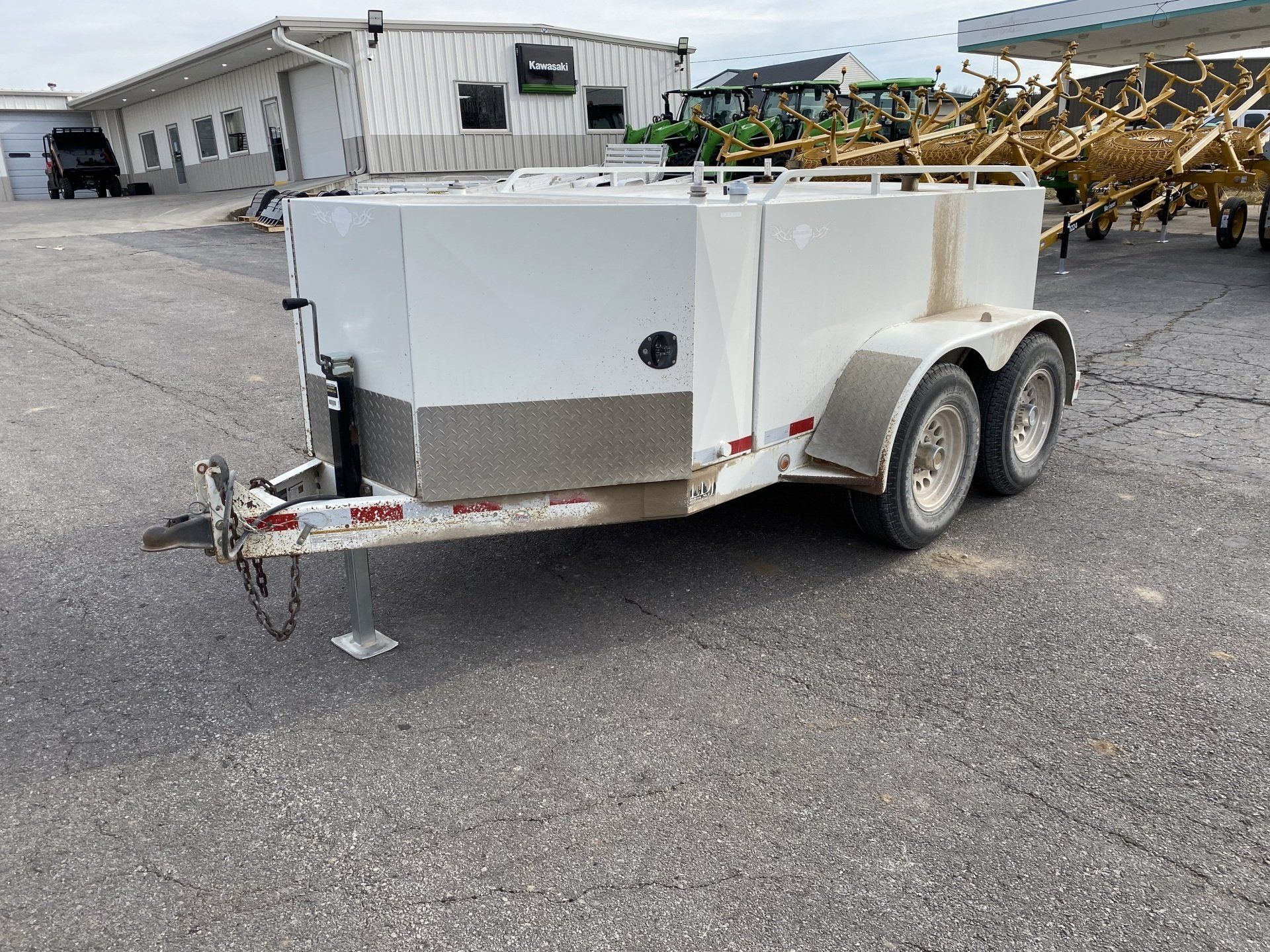 White fuel trailer with a silver front panel, parked on asphalt. A building and farm equipment are in the background.