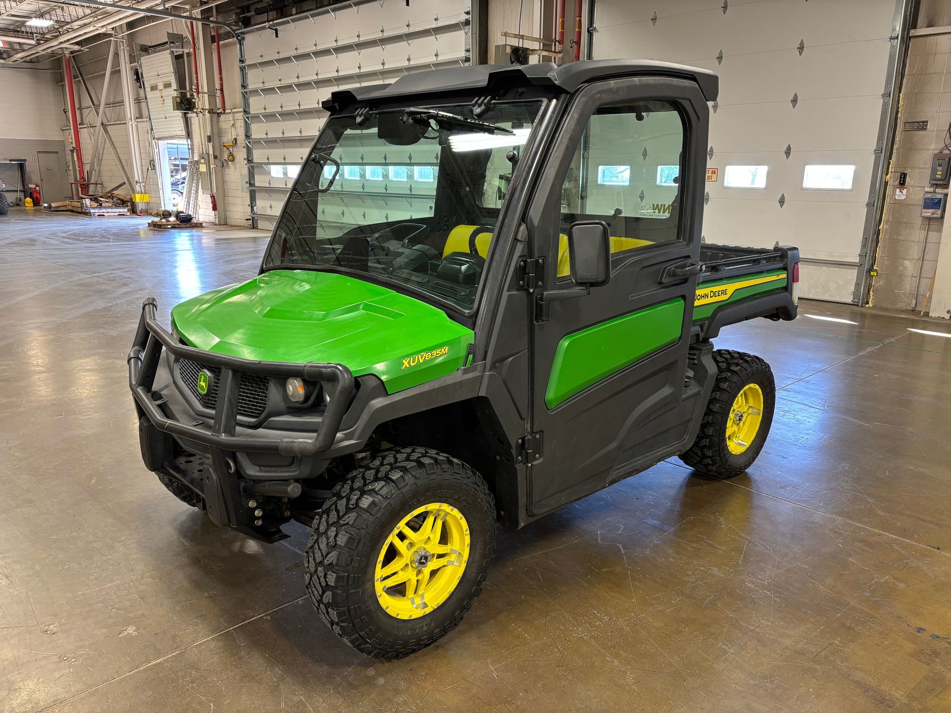 Green and yellow John Deere Gator utility vehicle with enclosed cab.