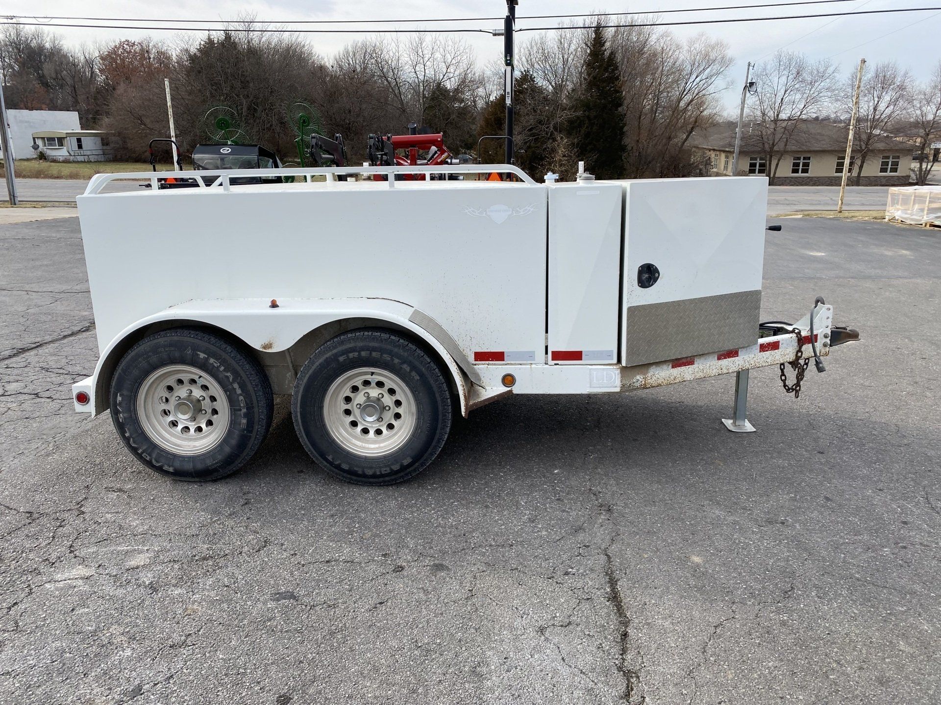 White fuel trailer with a silver front panel, parked on asphalt, side view shot.