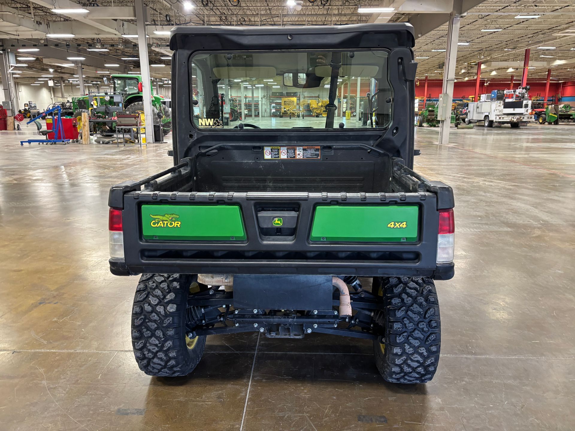 Rear view of a John Deere Gator utility vehicle with a black frame and a green bed, in a warehouse.