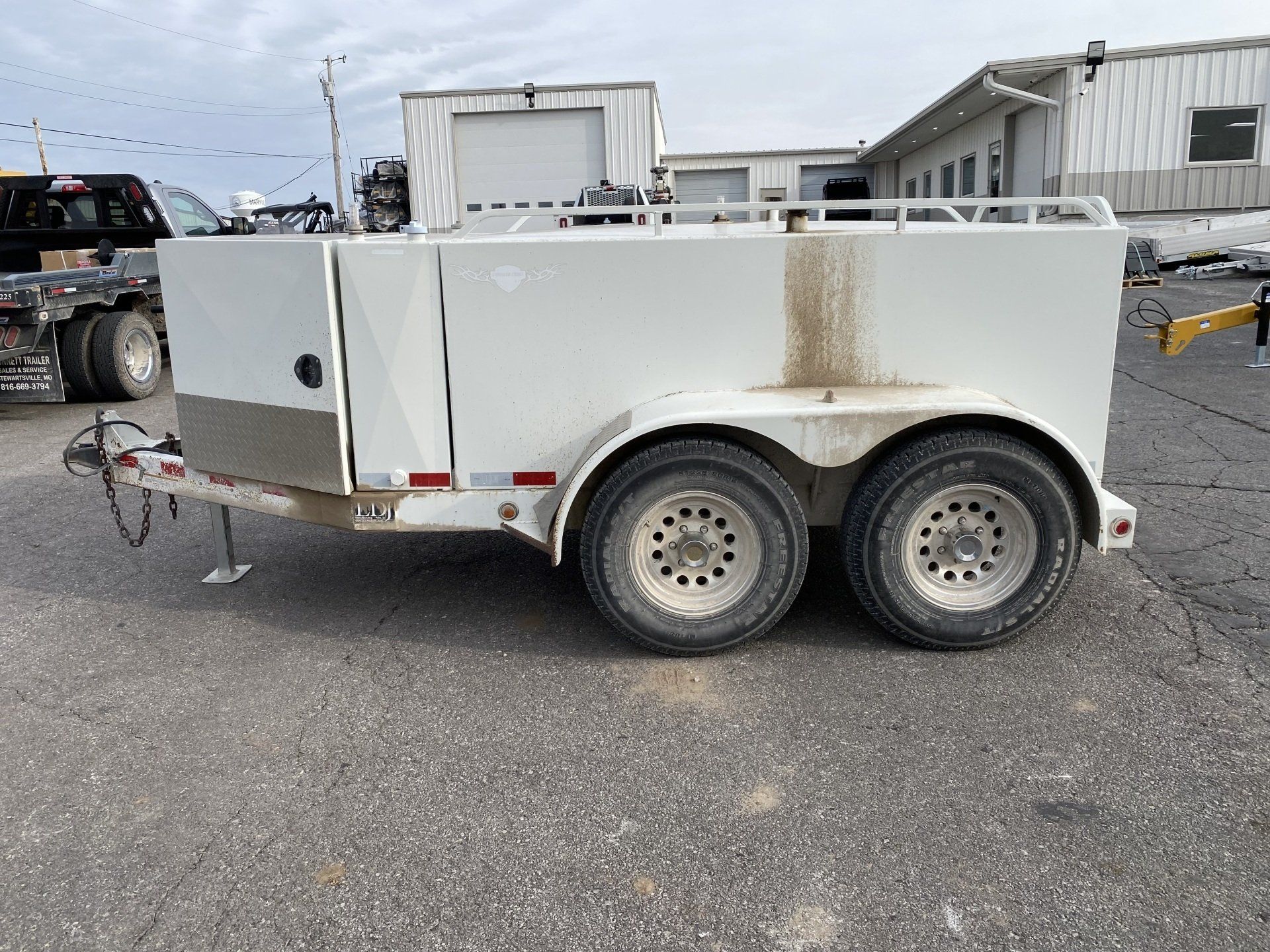White fuel trailer with a silver front panel, parked on asphalt, side view shot.