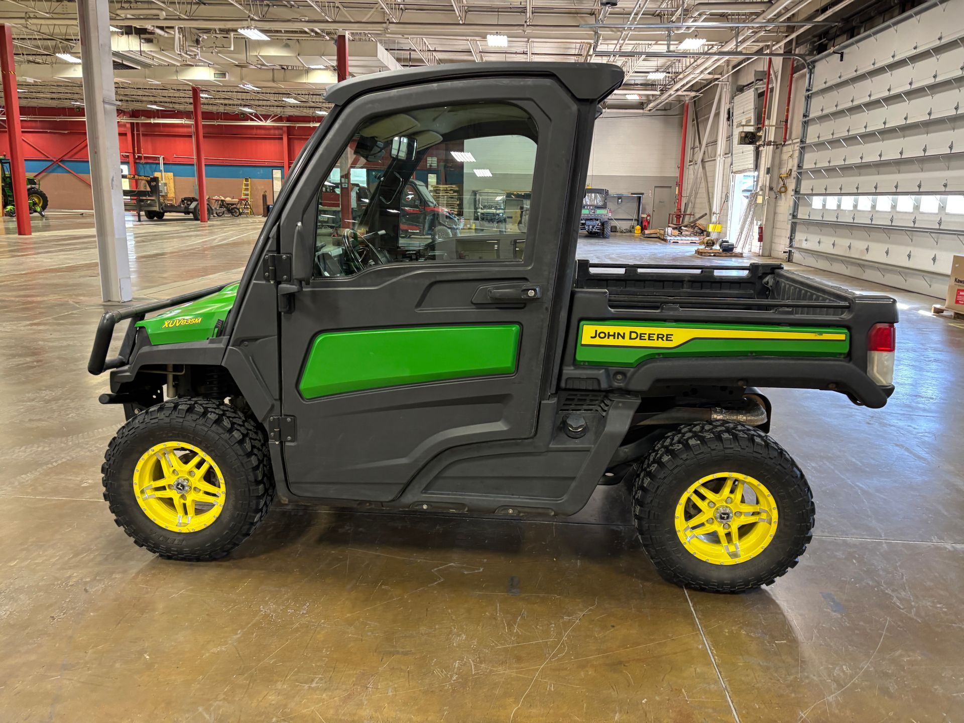 Green and black John Deere Gator utility vehicle with yellow wheels parked inside a building.