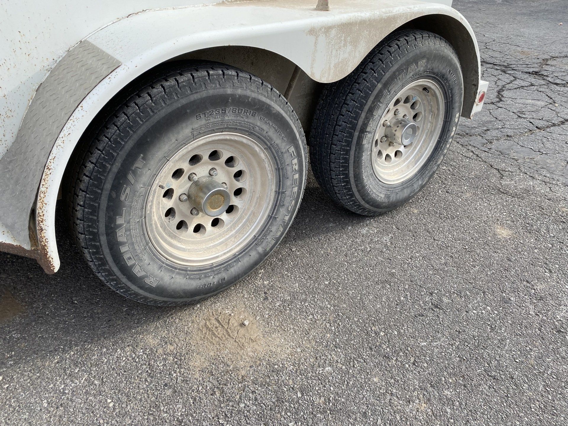 Two white trailer wheels on asphalt.