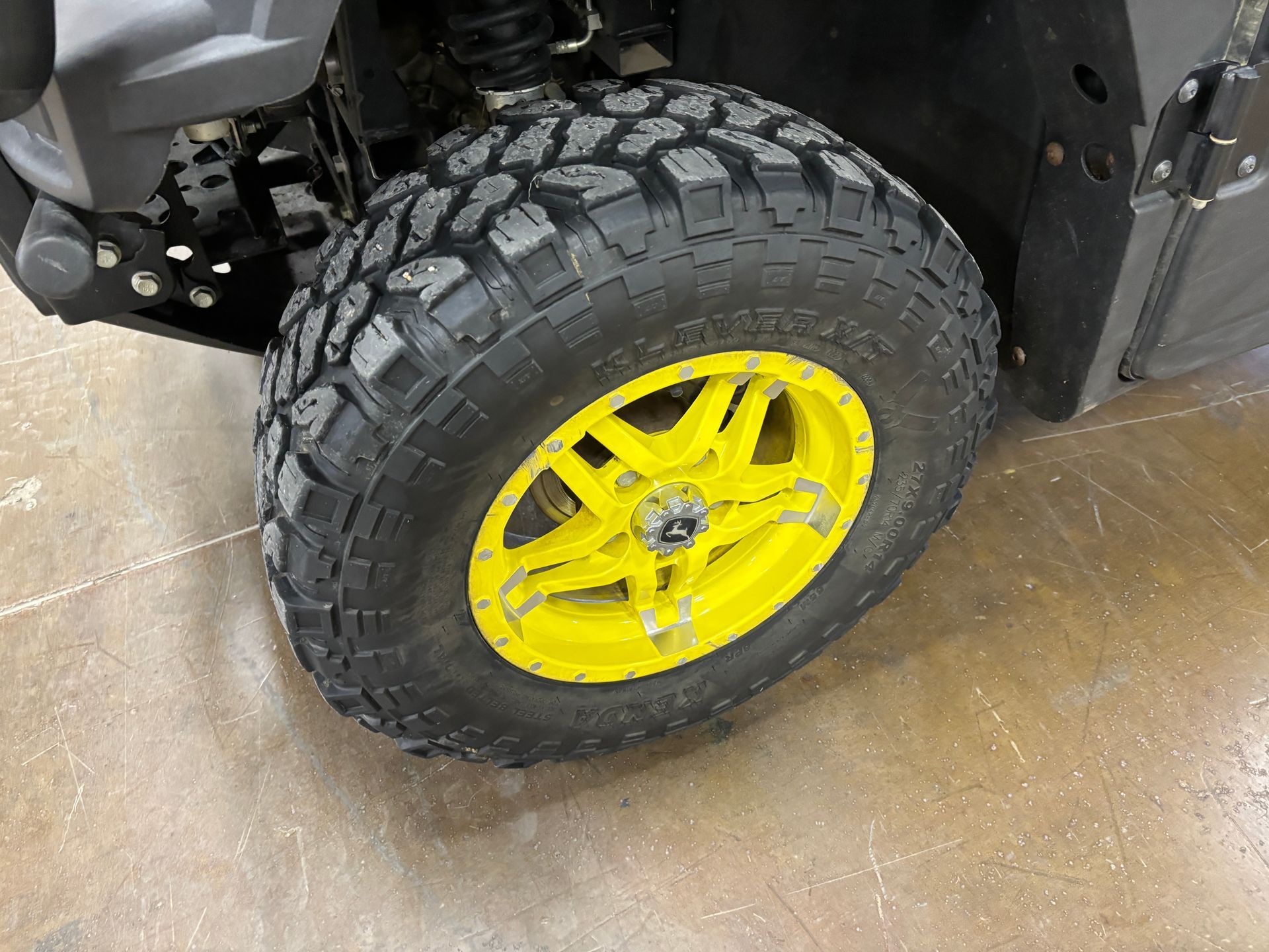 Off-road vehicle tire with black tread and yellow rim on a concrete floor.