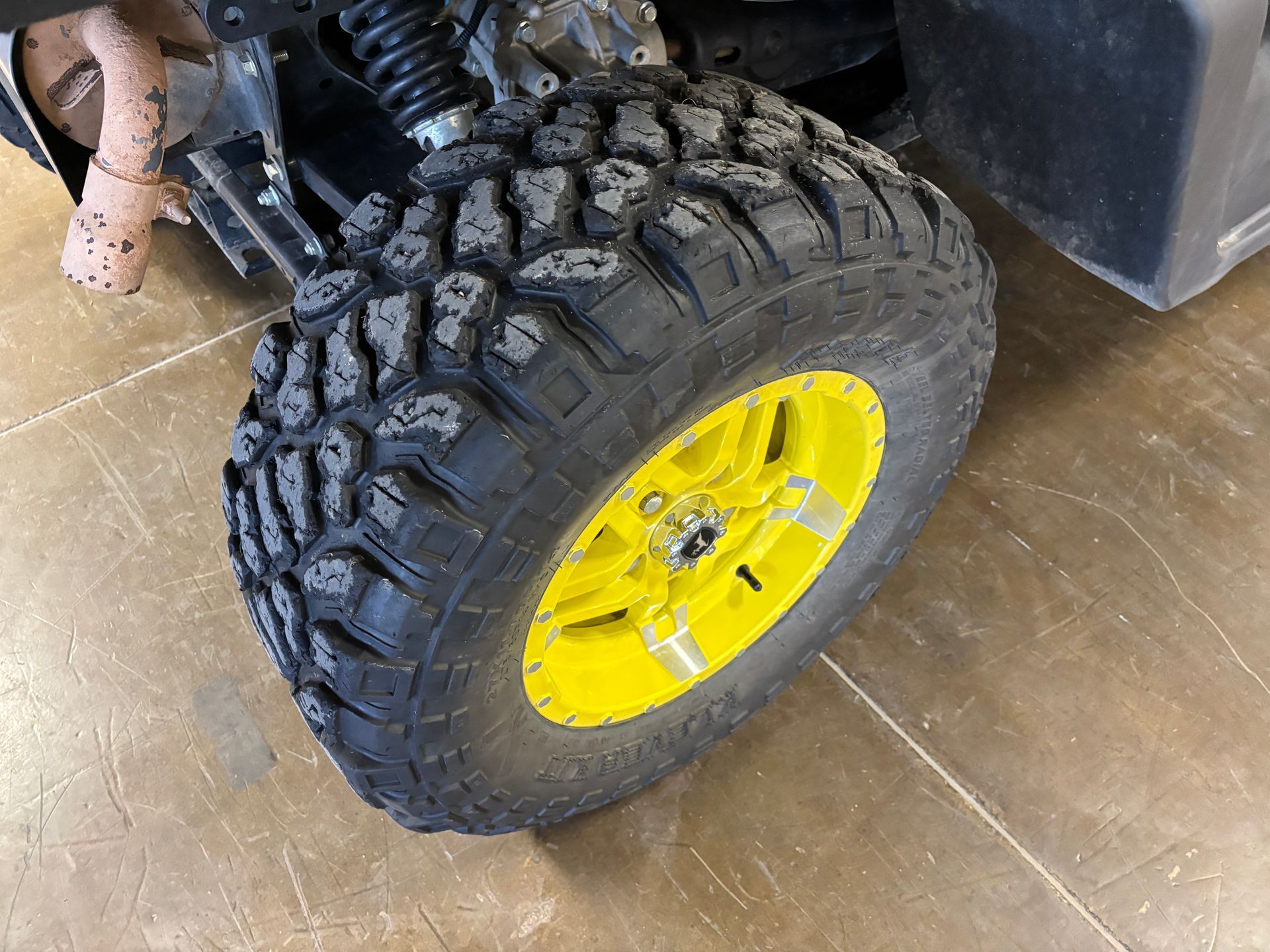 Close-up of a black off-road tire on a yellow rim, angled on a surface.