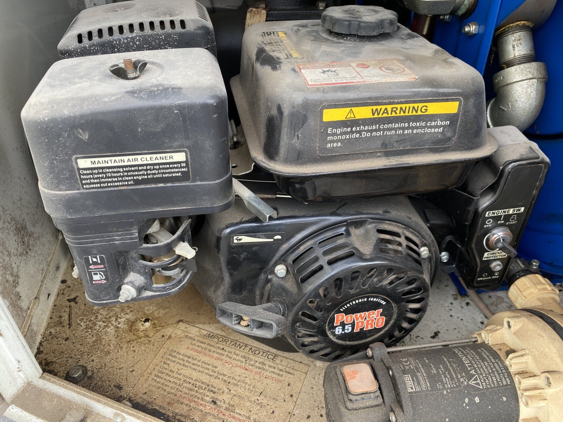 Close-up of a dusty, black engine with warning labels and other machine components.