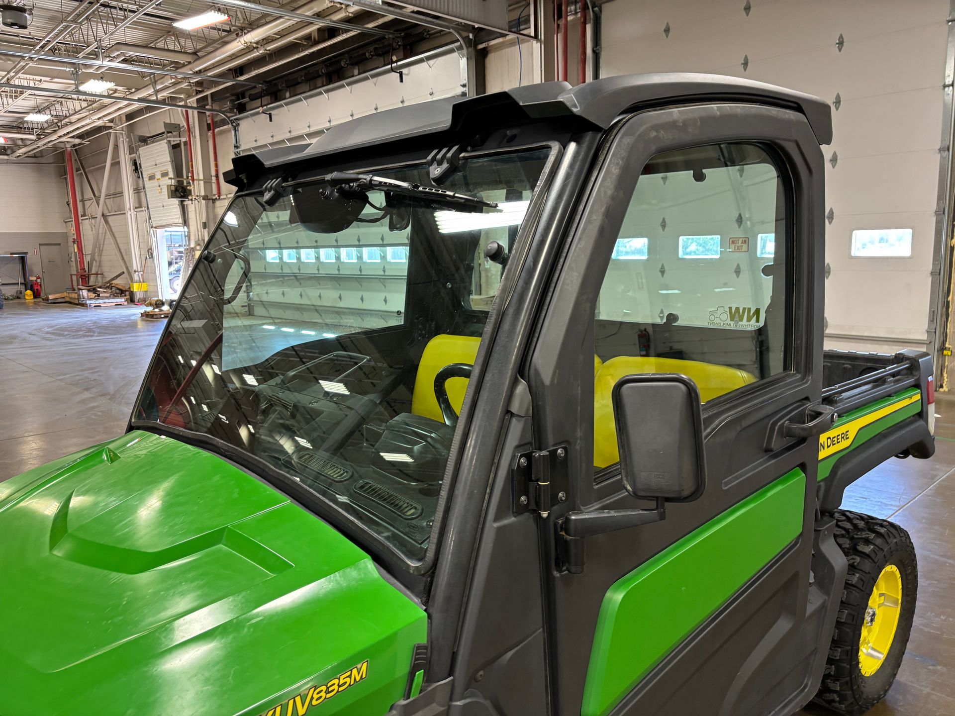 Green John Deere Gator utility vehicle with a cab, indoors.