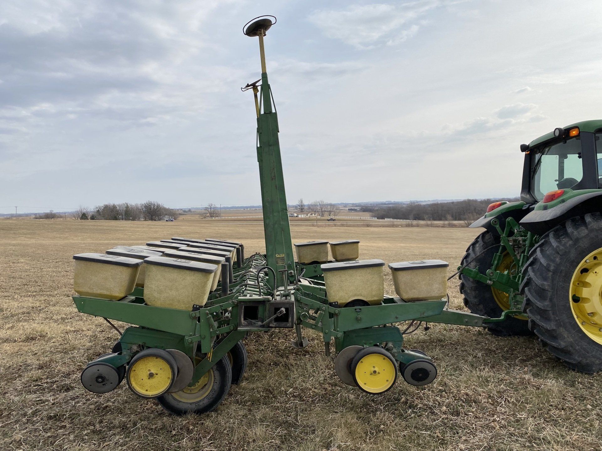 Green tractor pulling a planter in a field, with GPS antenna extended.