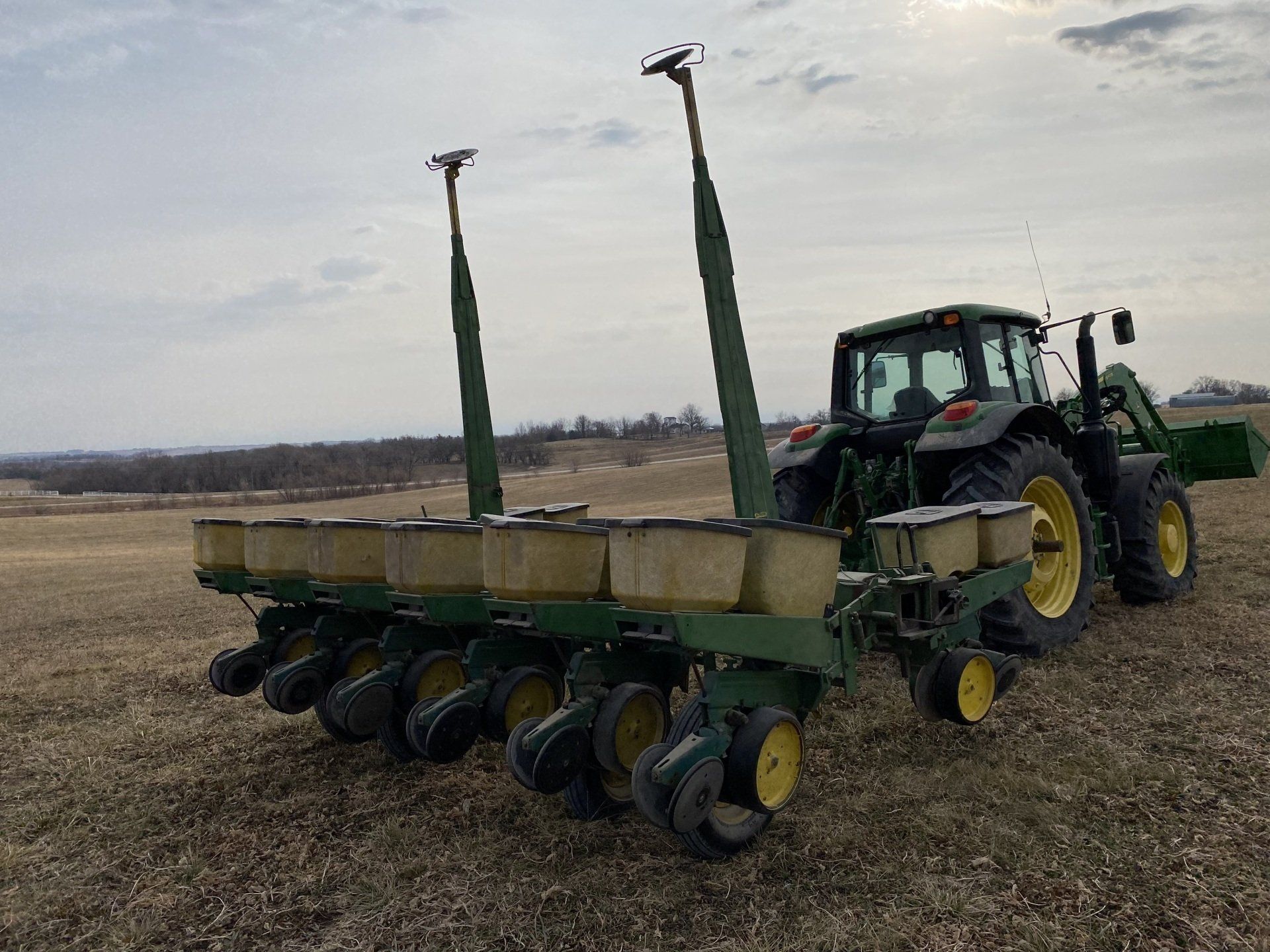 A green tractor pulling a planter in a field on a cloudy day.