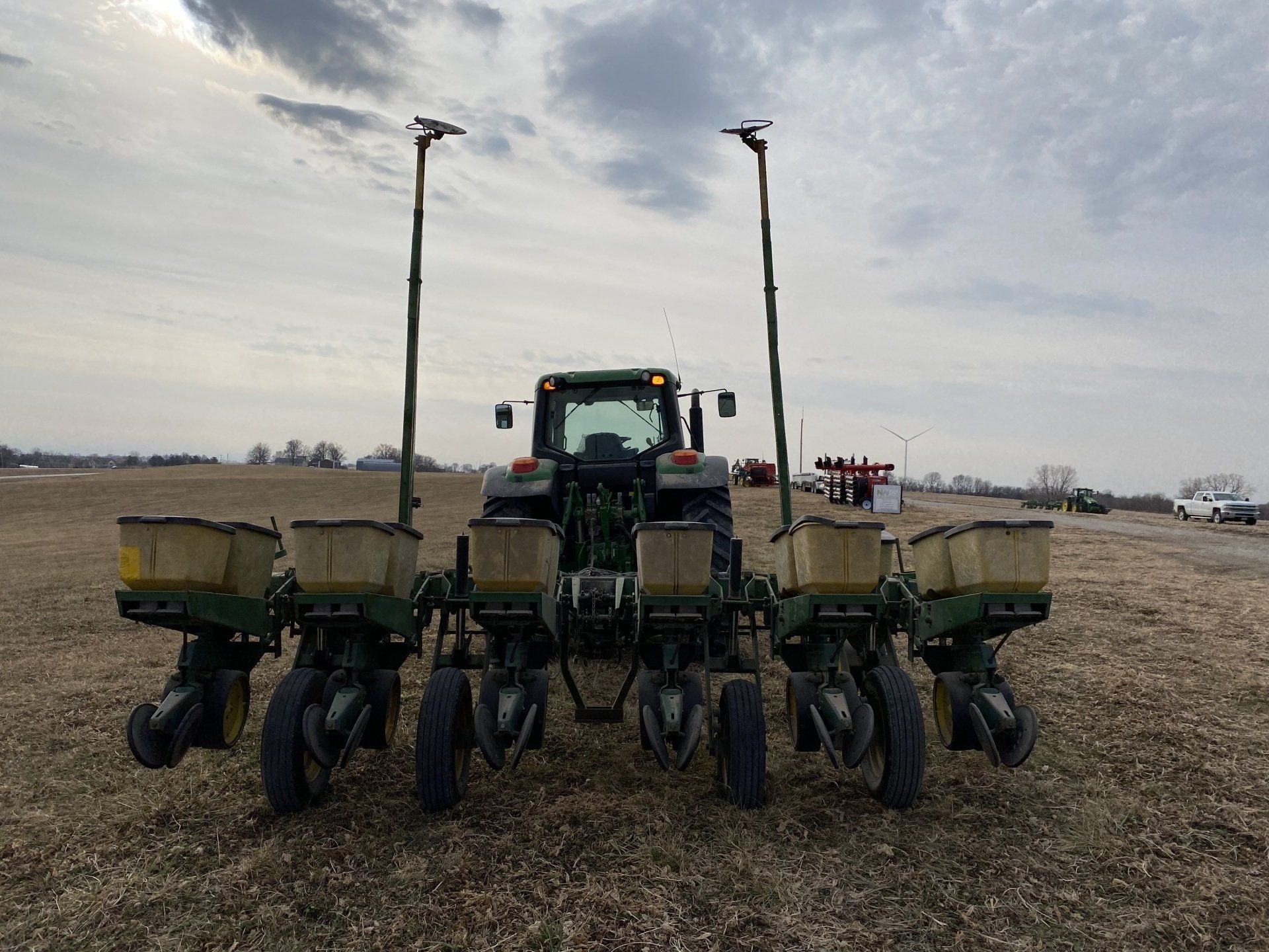 Green tractor pulling a planter in a field on a cloudy day.