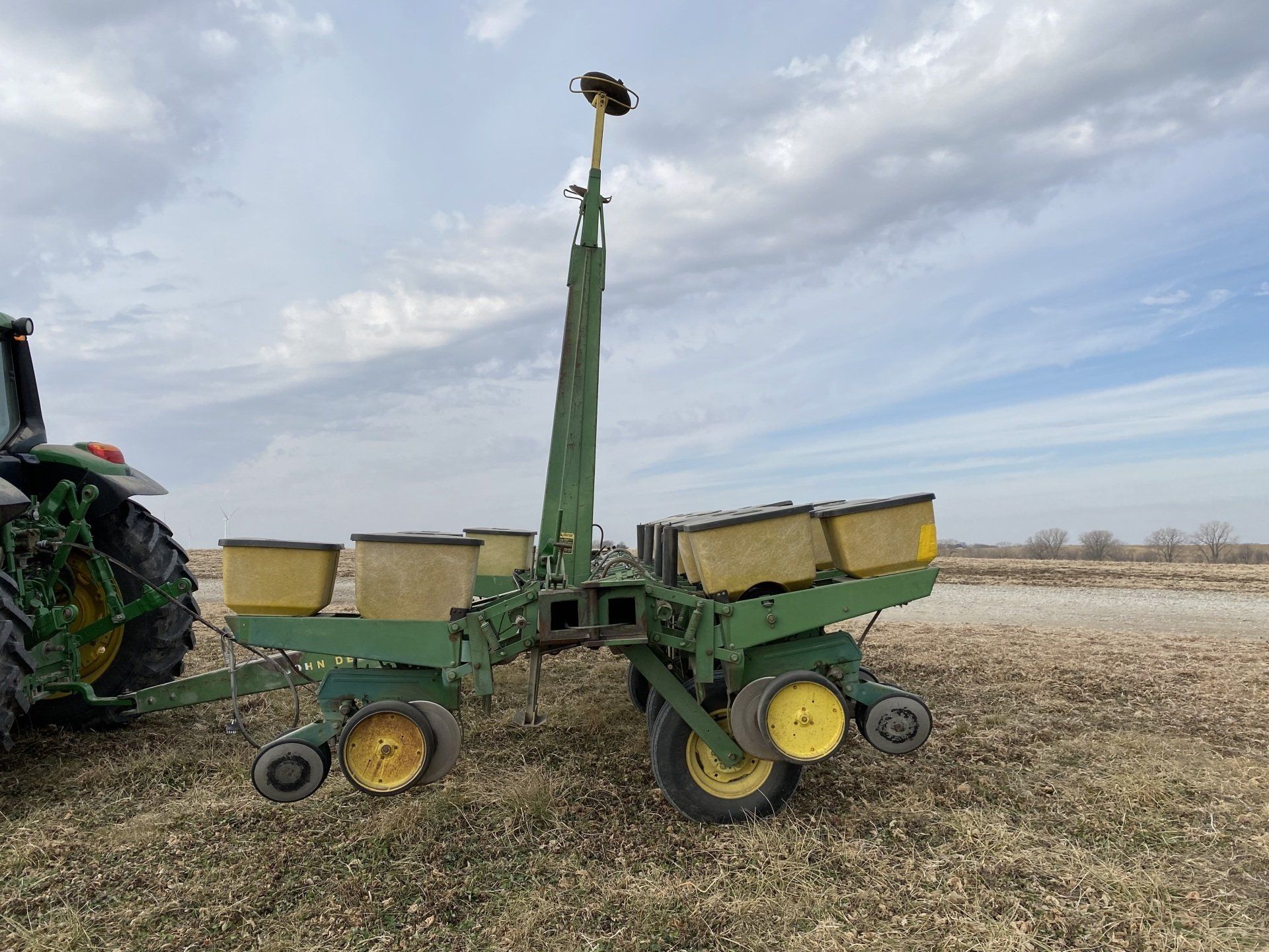 Green John Deere planter attached to a tractor in a field under a cloudy sky.