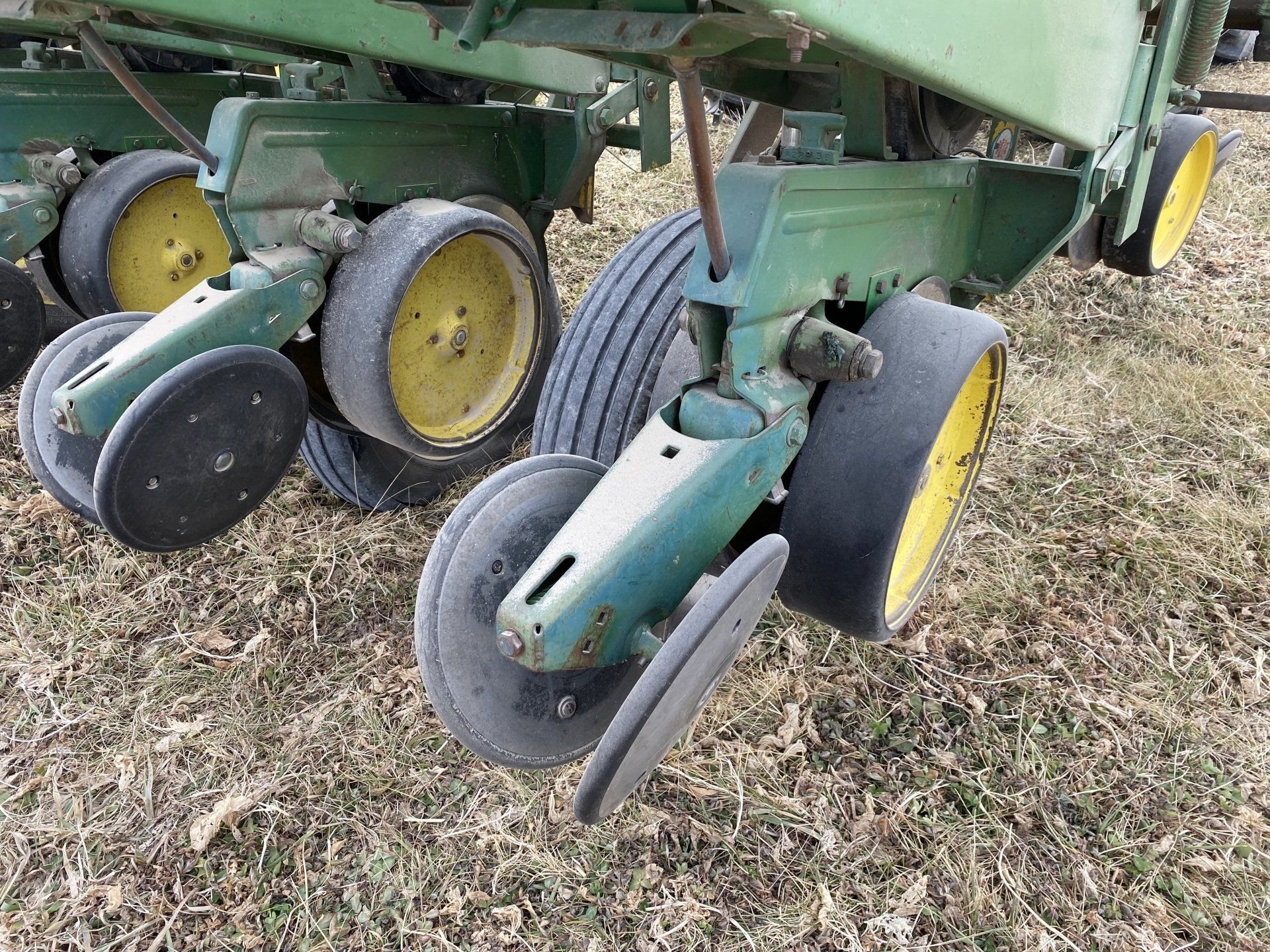 Green farm planter detail with black and yellow wheels and disc blades, outdoors on brown field.