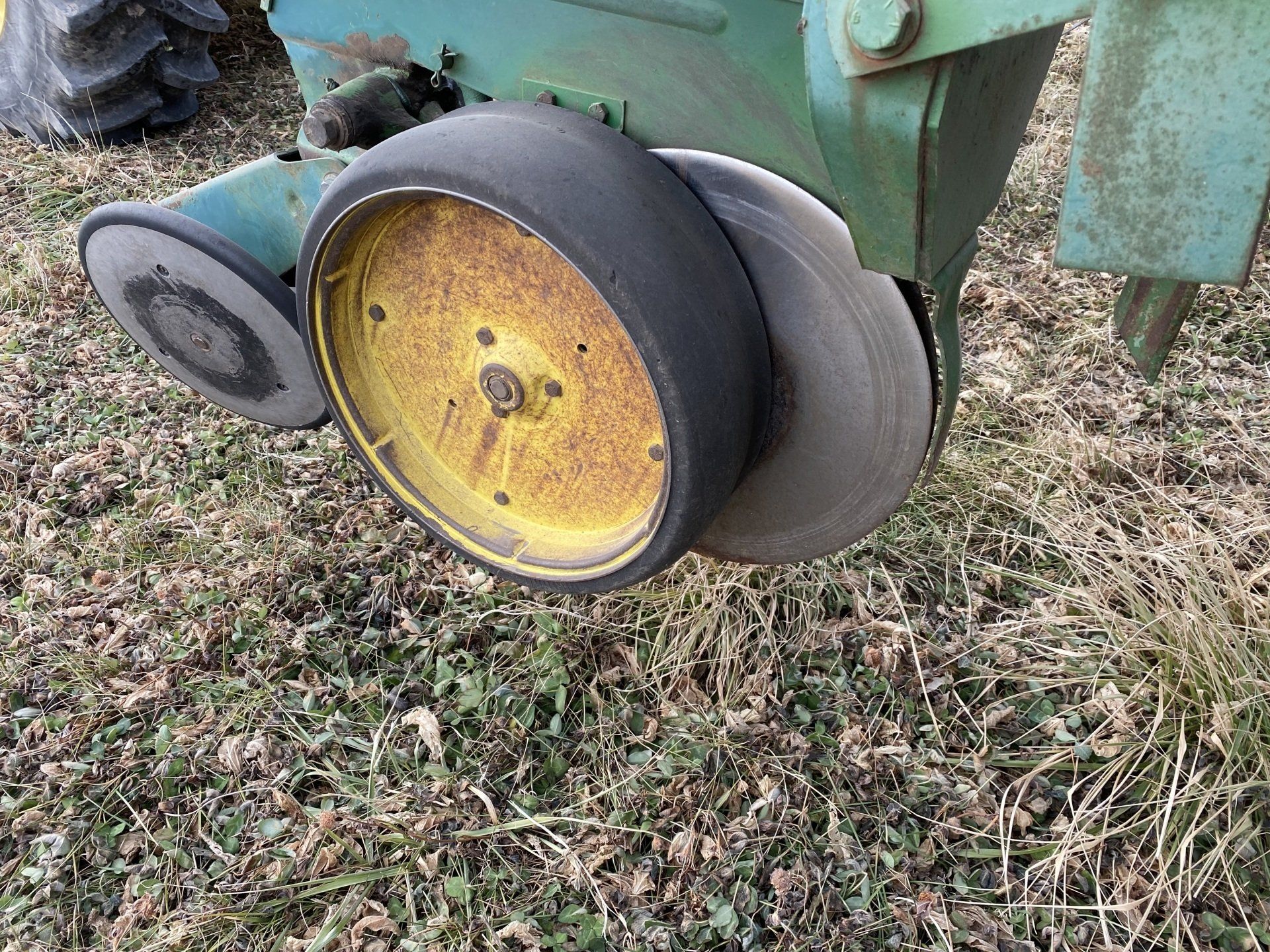 Two agricultural planters, green with gray and yellow wheels, sit in a field.
