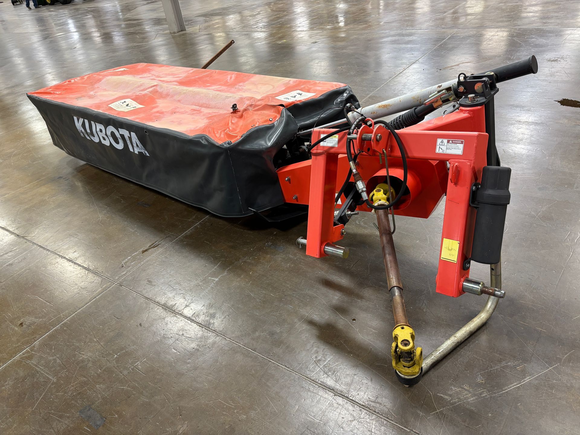 Kubota disc mower, in a orange and black cover, on a concrete floor, angled shot.