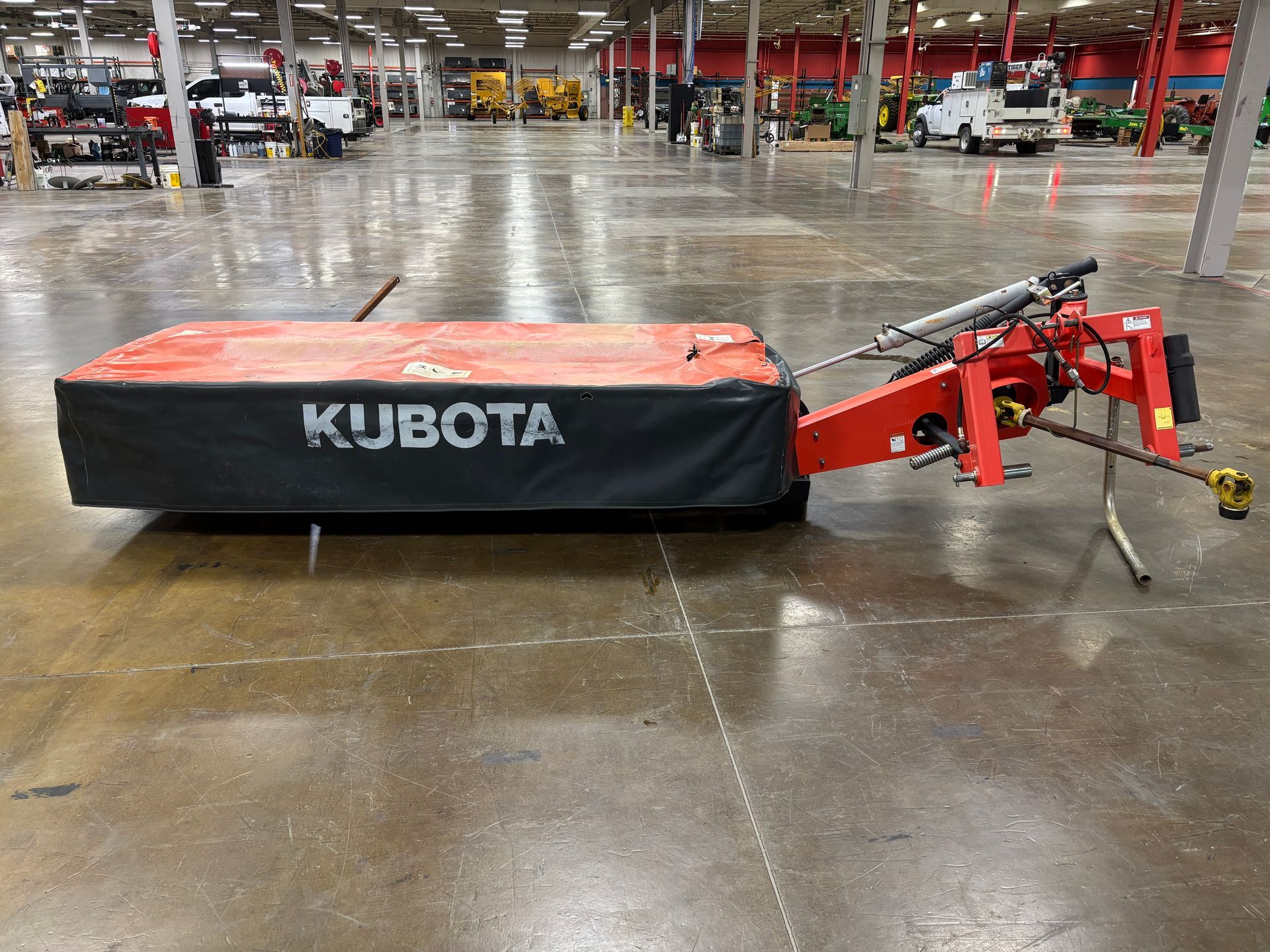 Kubota disc mower, in a orange and black cover, on a concrete floor, side view.