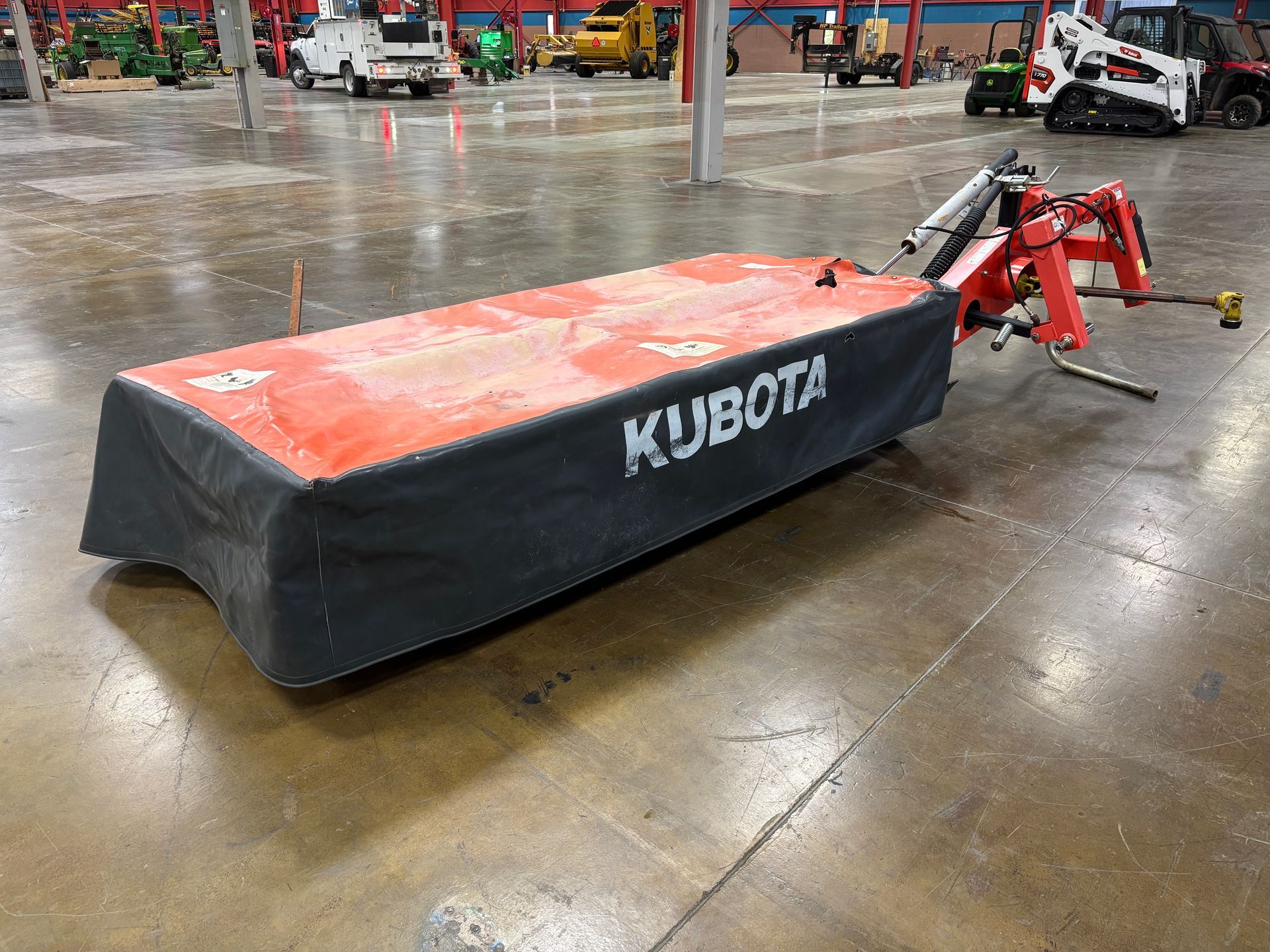 Kubota disc mower, in a orange and black cover, on a concrete floor, angled view.