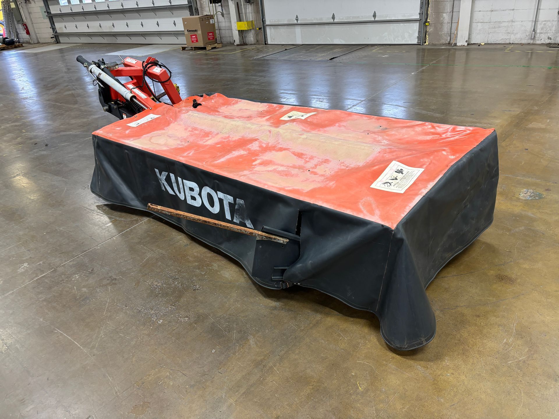 Kubota disc mower, in a orange and black cover, on a concrete floor, angled view.