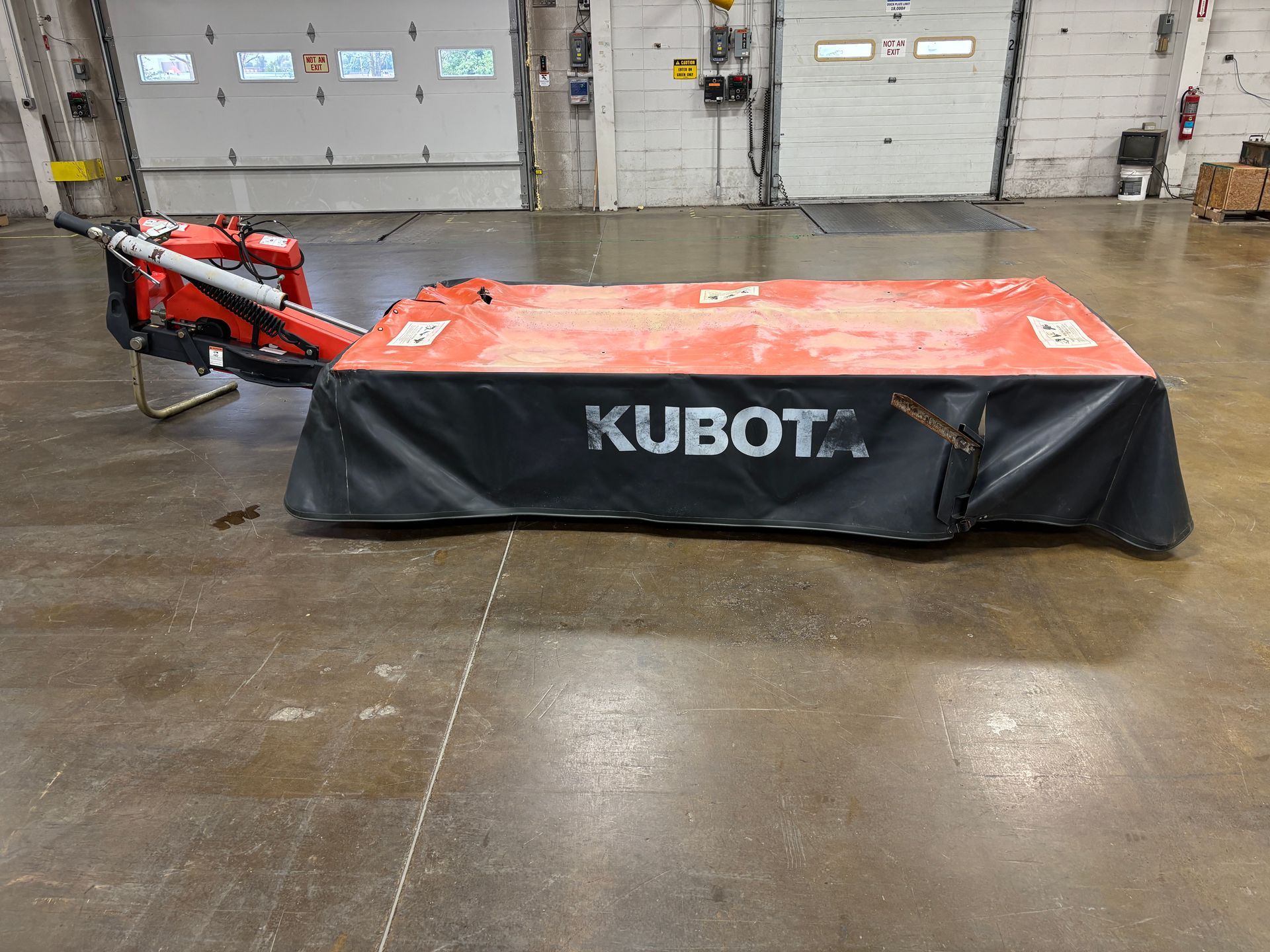 Kubota disc mower, in a orange and black cover, on a concrete floor, back view.