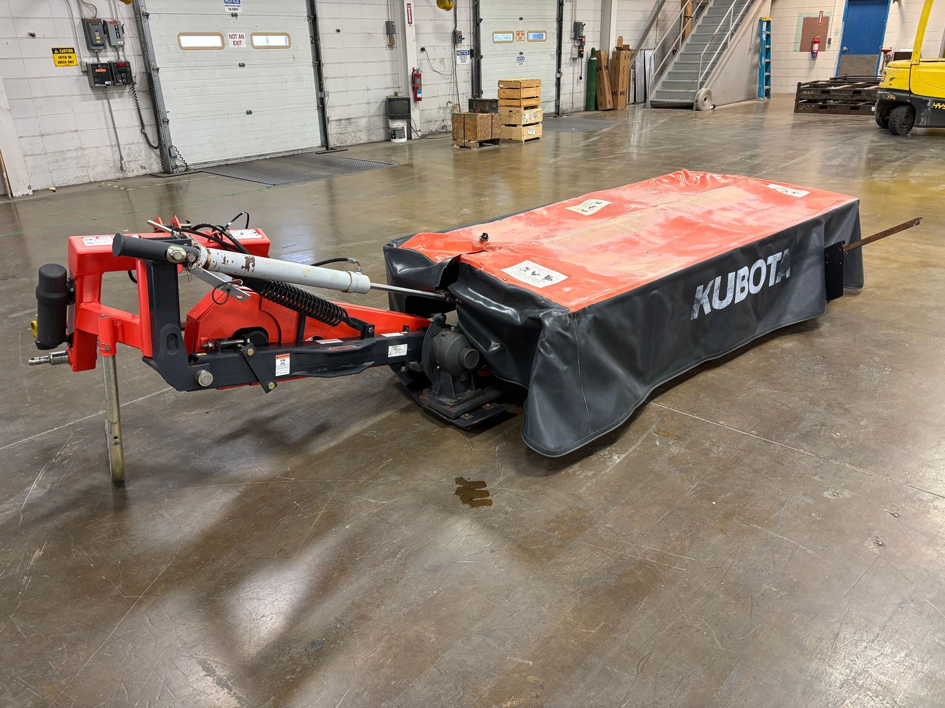 Kubota disc mower, in a orange and black cover, on a concrete floor, angled view.