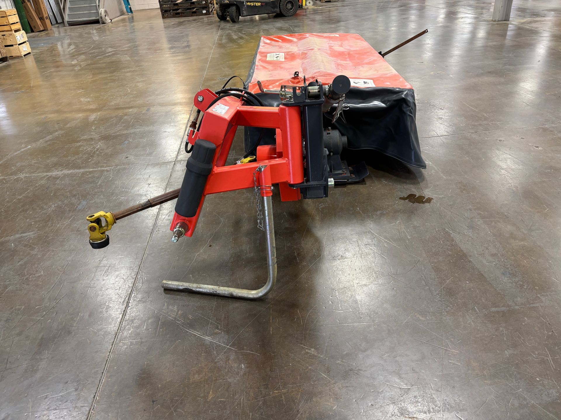 Kubota disc mower, in a orange and black cover, on a concrete floor, side view.