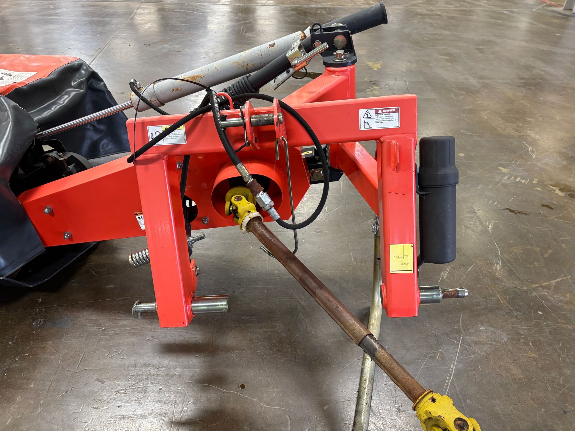 Orange farm equipment's rear with rotating shaft and hydraulic lines. Metal frame, black details, and yellow connection.