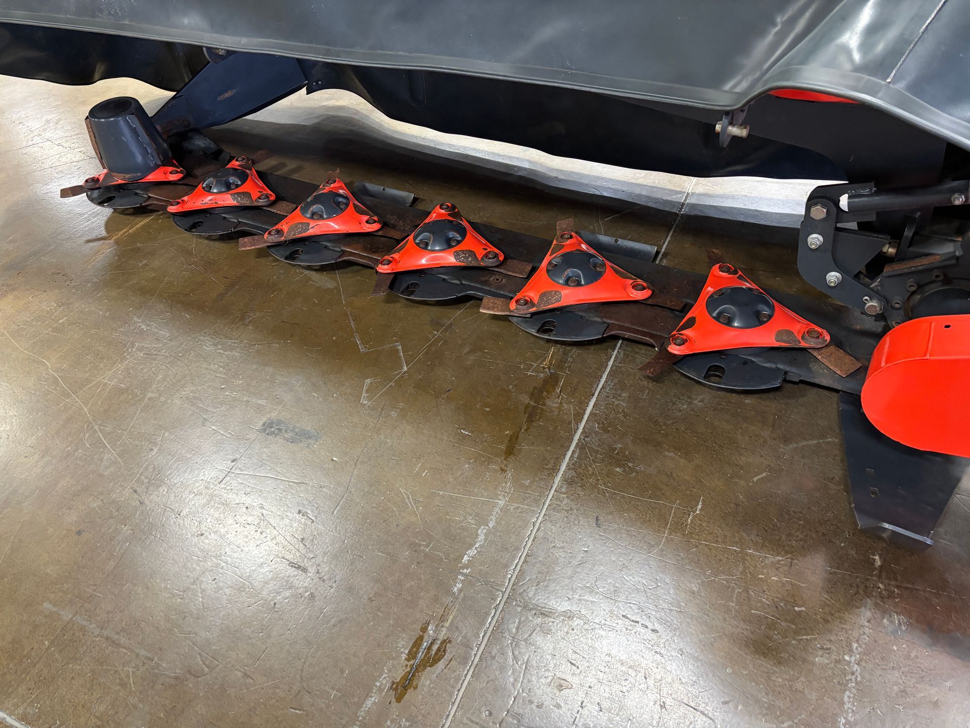 Close-up of Kubota disc mower with orange protective covers and black blades on a concrete surface.