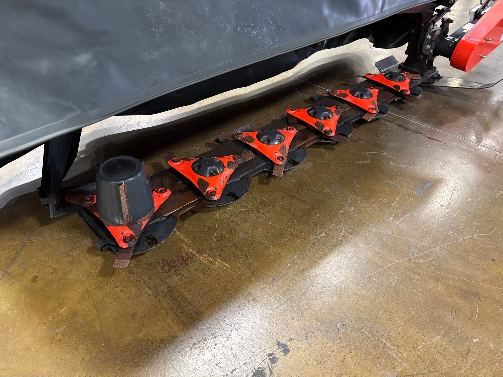 Close-up of Kubota disc mower with orange protective covers and black blades on a concrete surface.