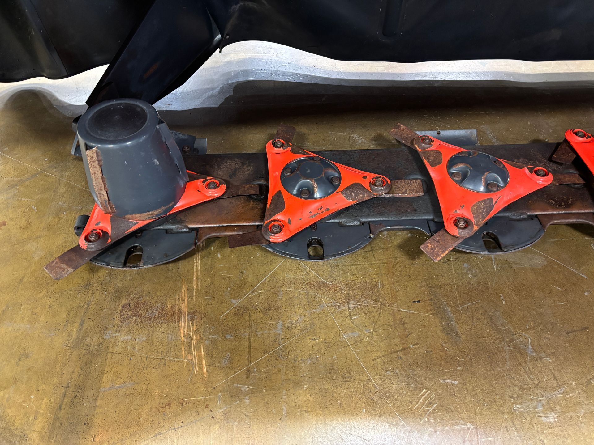 Close-up of Kubota disc mower with orange protective covers and black blades on a concrete surface.