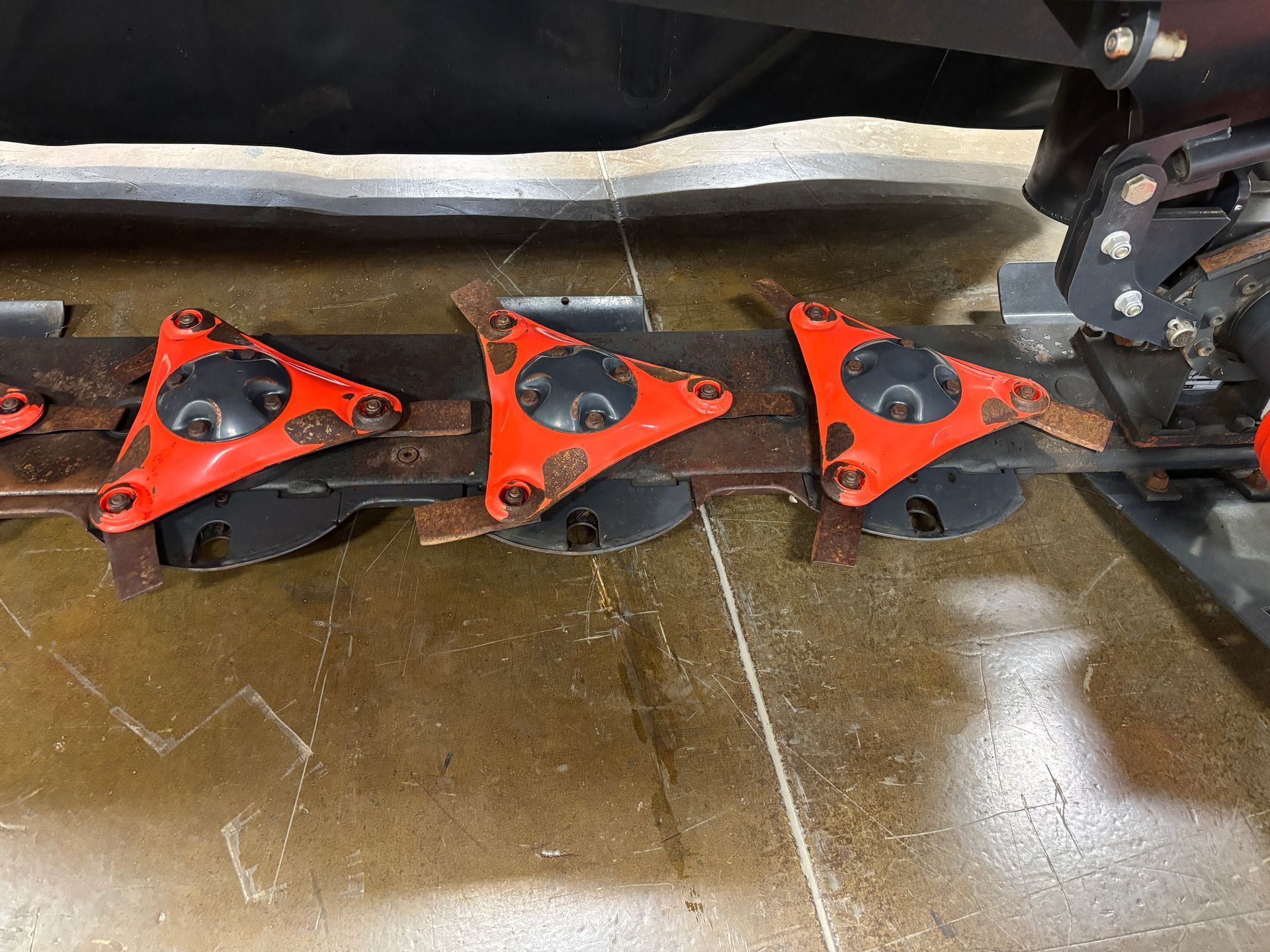 Close-up of Kubota disc mower with orange protective covers and black blades on a concrete surface.