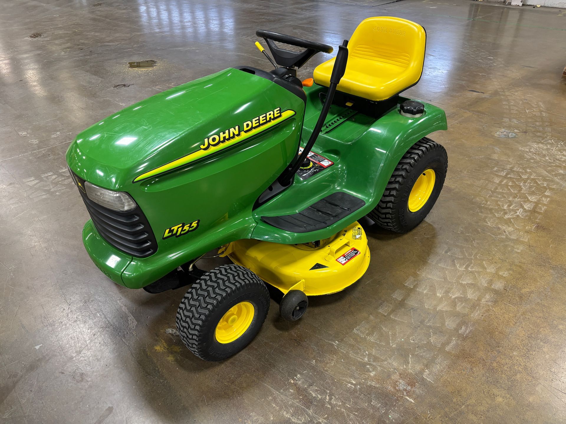 Green John Deere riding lawn mower with yellow accents on a gray floor.
