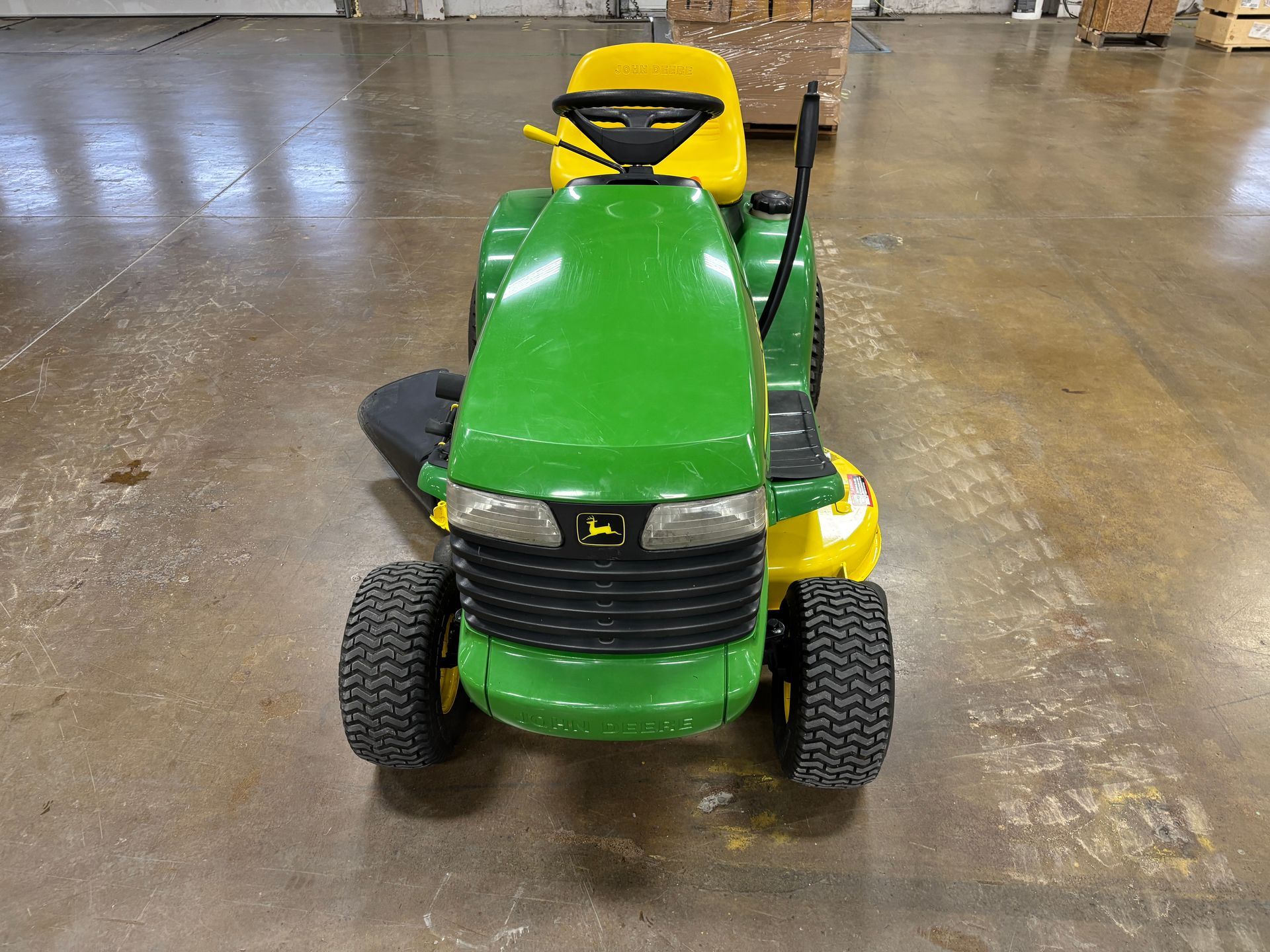 Green and yellow John Deere riding lawn mower on a concrete surface.