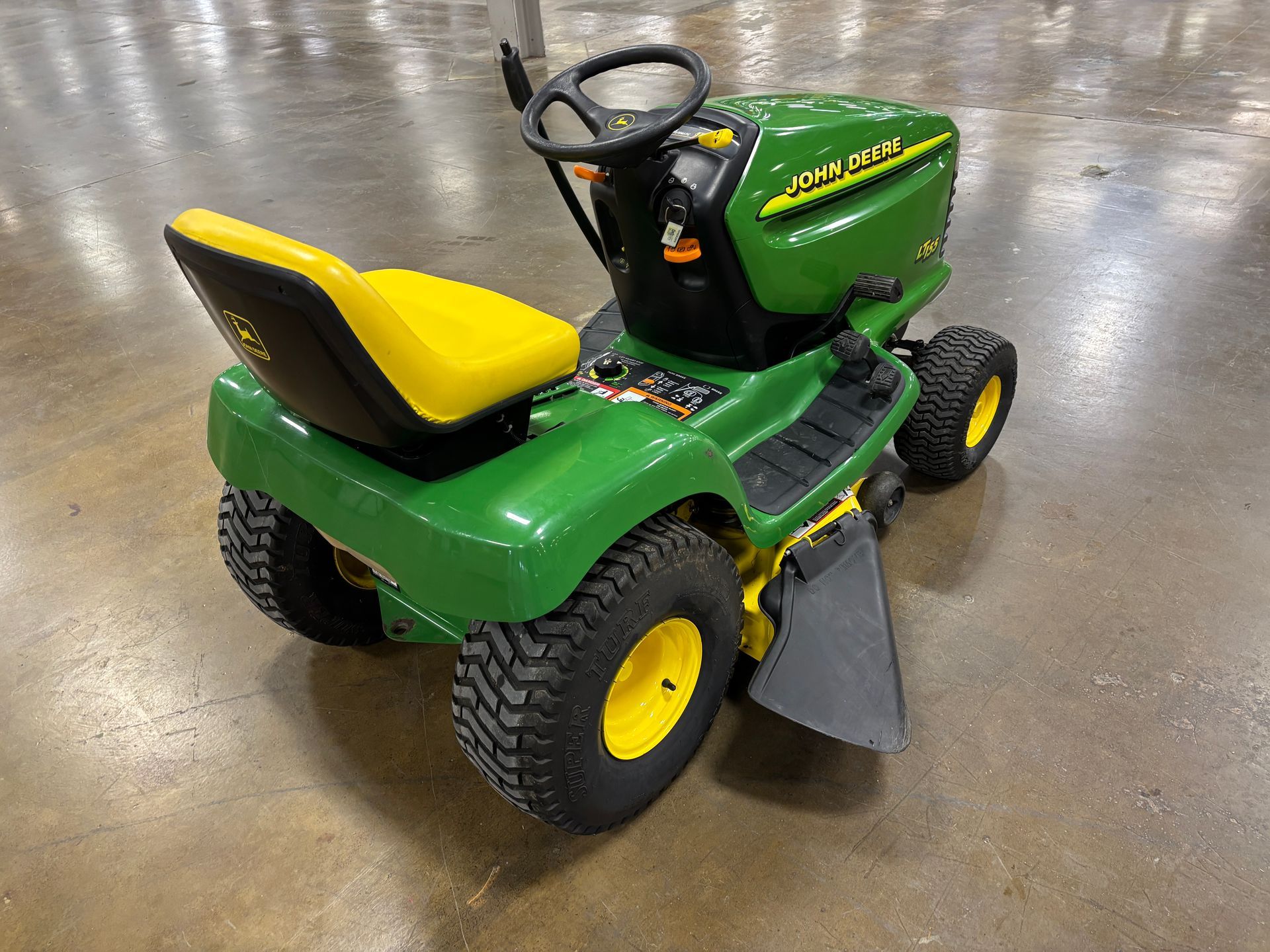 Green and yellow John Deere riding lawn mower on a concrete floor.
