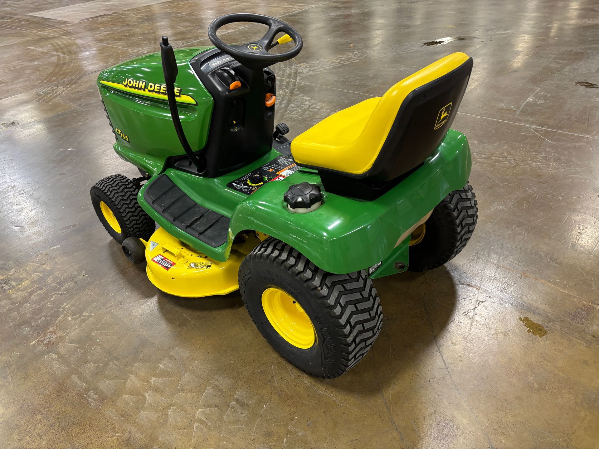 Green and yellow John Deere riding lawn mower on a concrete floor.