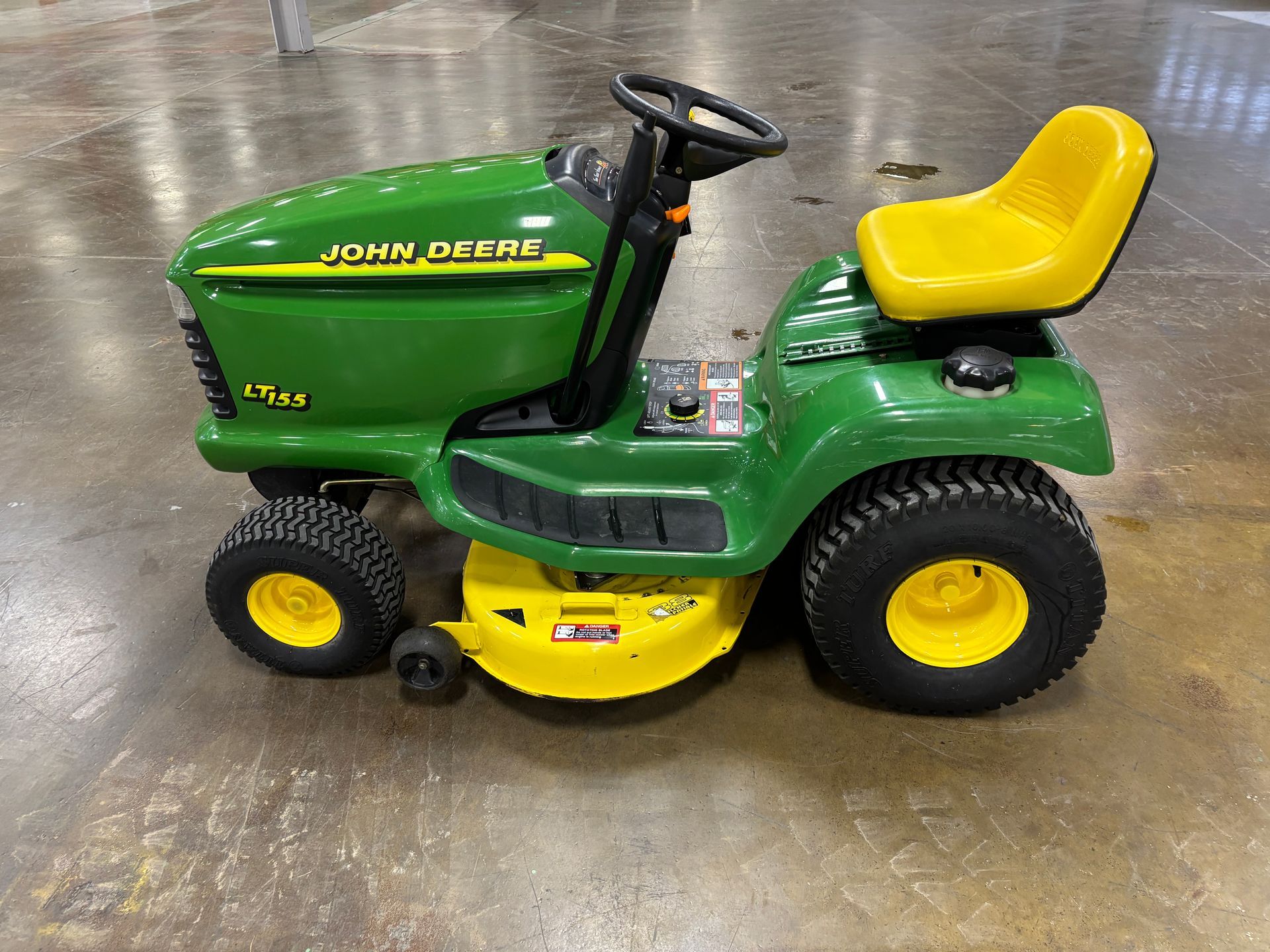Green and yellow John Deere riding lawnmower with a yellow seat and wheels, on a gray floor.