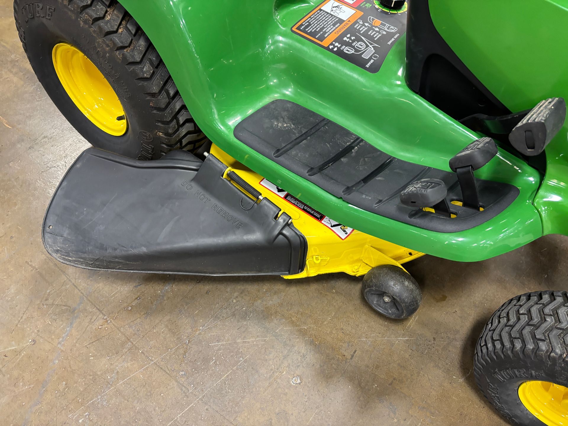 Yellow lawnmower deck under a green tractor.
