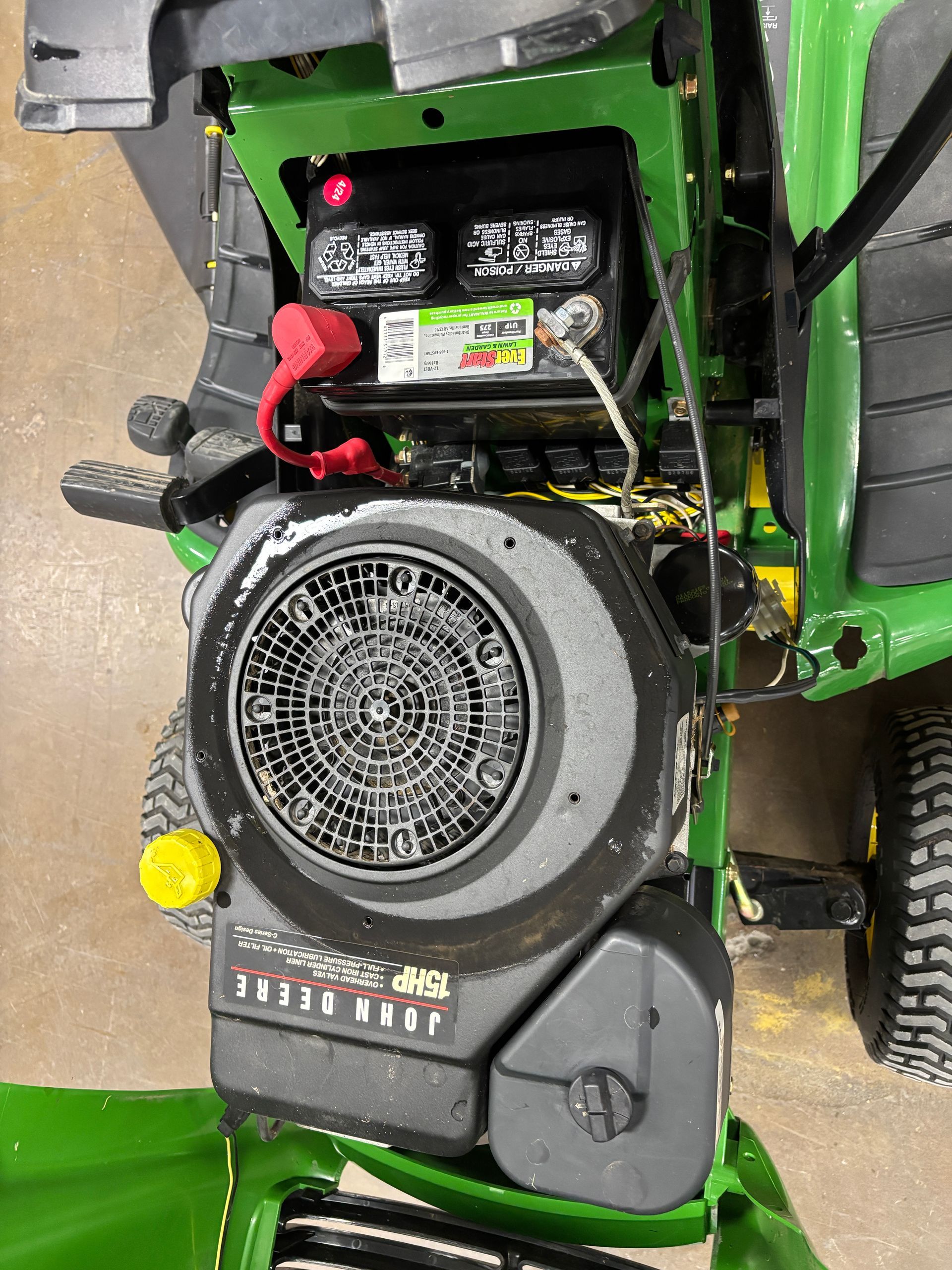 Top-down view of a John Deere riding mower engine with a battery and air filter.