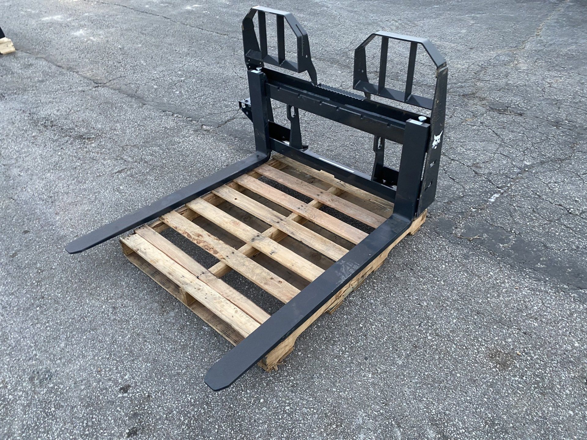Forklift attachment with forks inserted into a wooden pallet, outdoors.