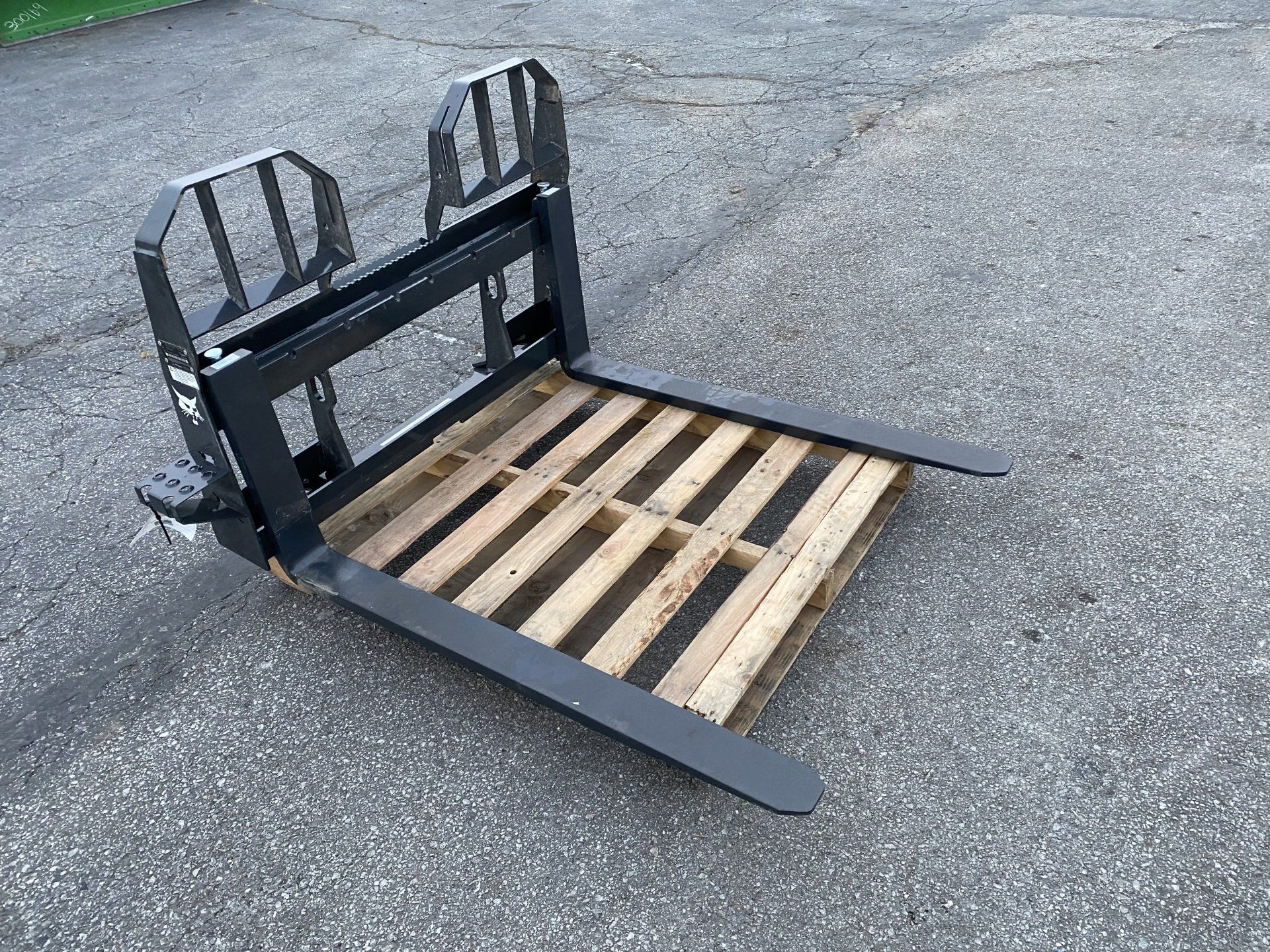 Black forklift attachment with pallet on asphalt.